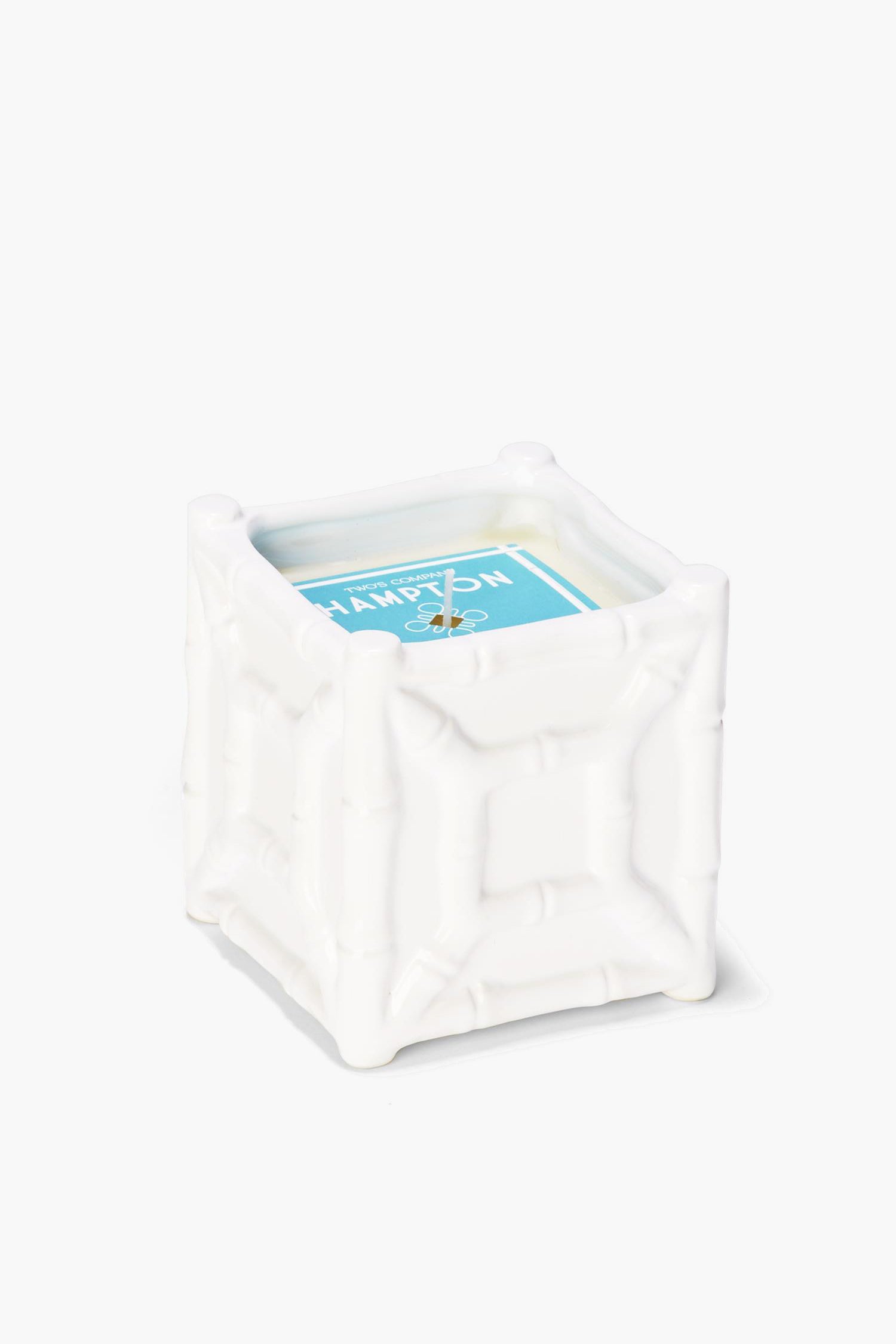 A white, square bamboo candle holder by Two's Company with a textured chinoiserie design, featuring a sea spray scent candle with a blue label.