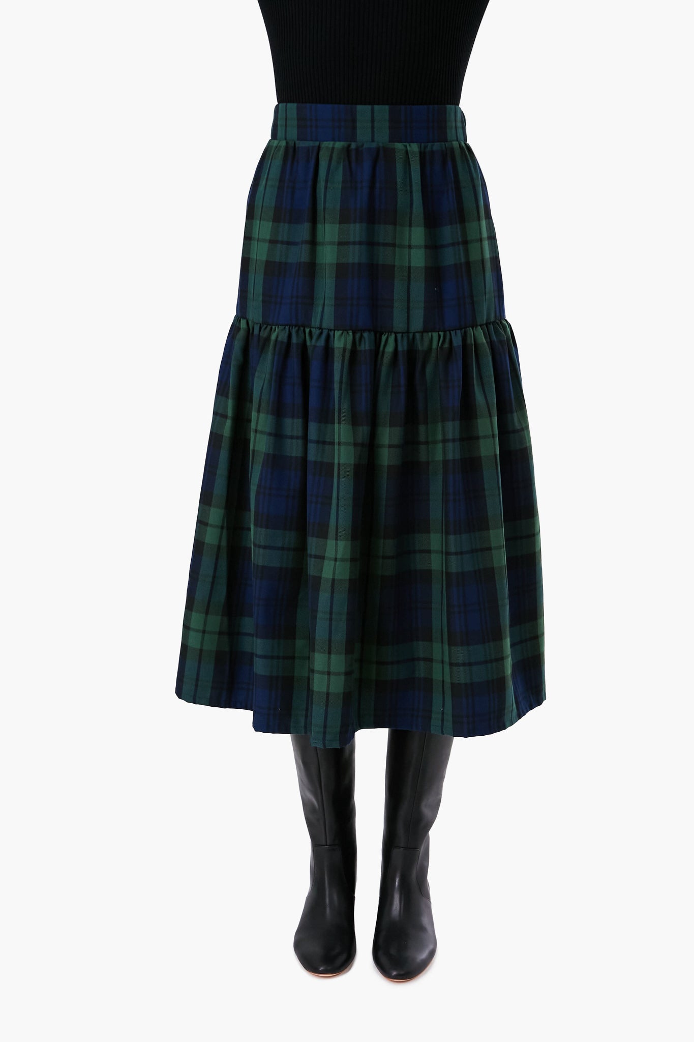 A person wearing a Nina Blanc black top, a handmade green and navy tartan midi skirt, and black knee-high boots.