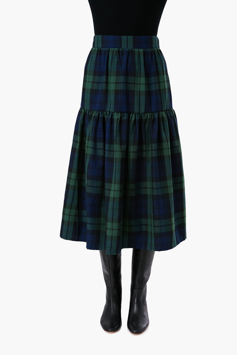 A person wearing a Nina Blanc black top, a handmade green and navy tartan midi skirt, and black knee-high boots.