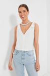 Woman wearing an Emerson Fry white linen crop top with adjustable tie shoulder straps, styled with light blue high-waisted jeans and a chunky beaded necklace.