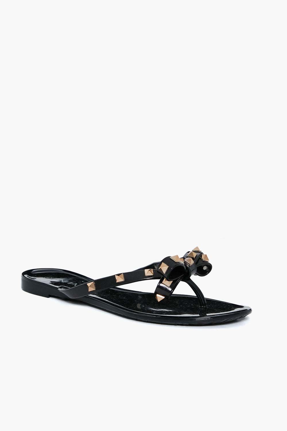 The Anina black thong sandals feature a flat sole, bow detail, and gold pyramid studs on the straps. These jelly bowtie sandals add a trendy, stylish touch to any outfit.