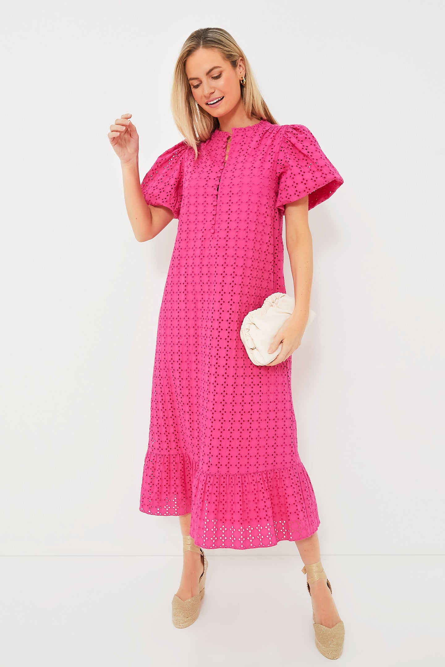 A woman wears a Hyacinth House Pink Eyelet Midi Dress with puff sleeves and beige espadrille wedges, holding a light-colored clutch.