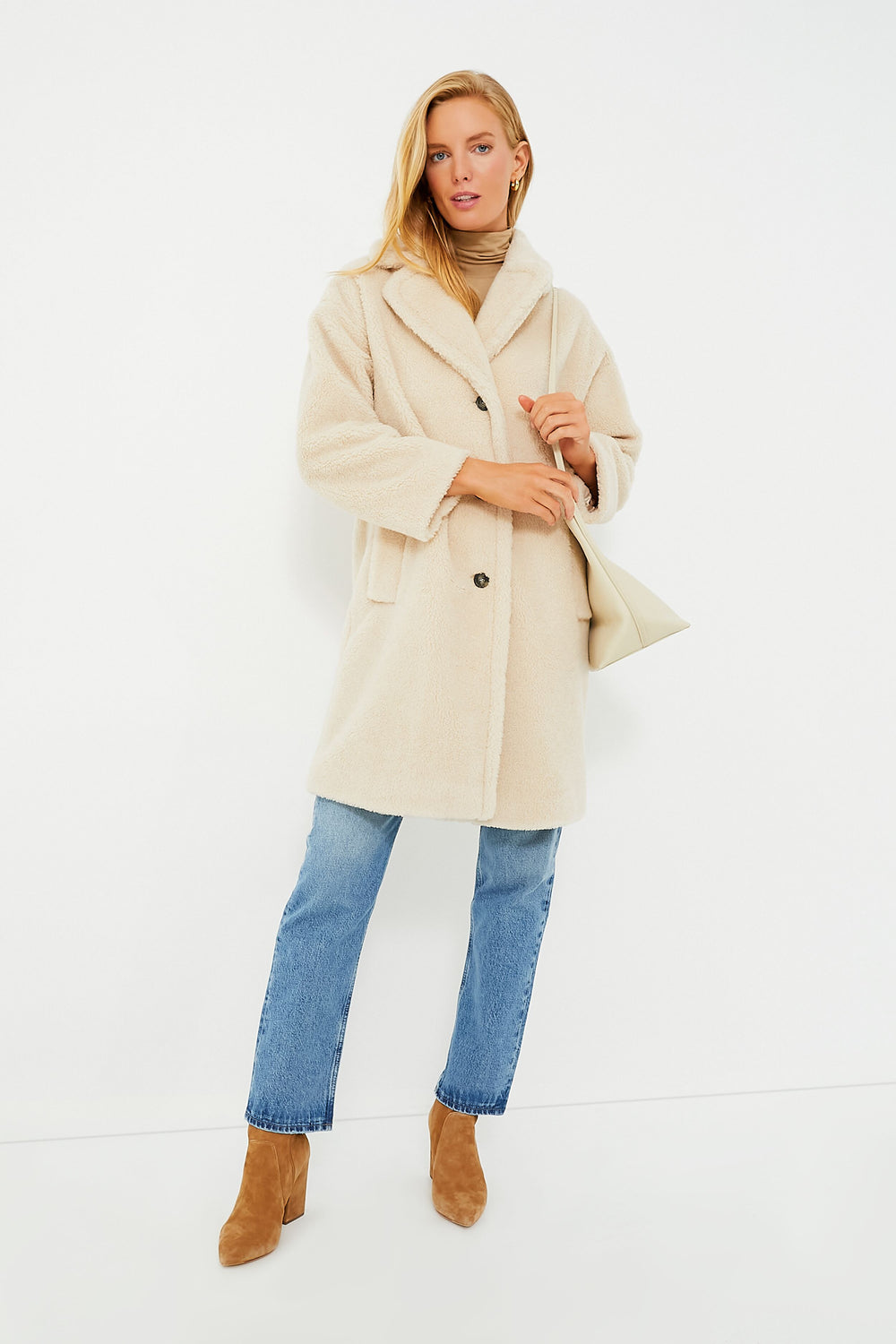 A person wears a beige sherpa coat from Weekend Max Mara, blue jeans, brown heeled boots, a tan top, and carries a cream shoulder bag—embodying the elegance of this Italian lifestyle brand.