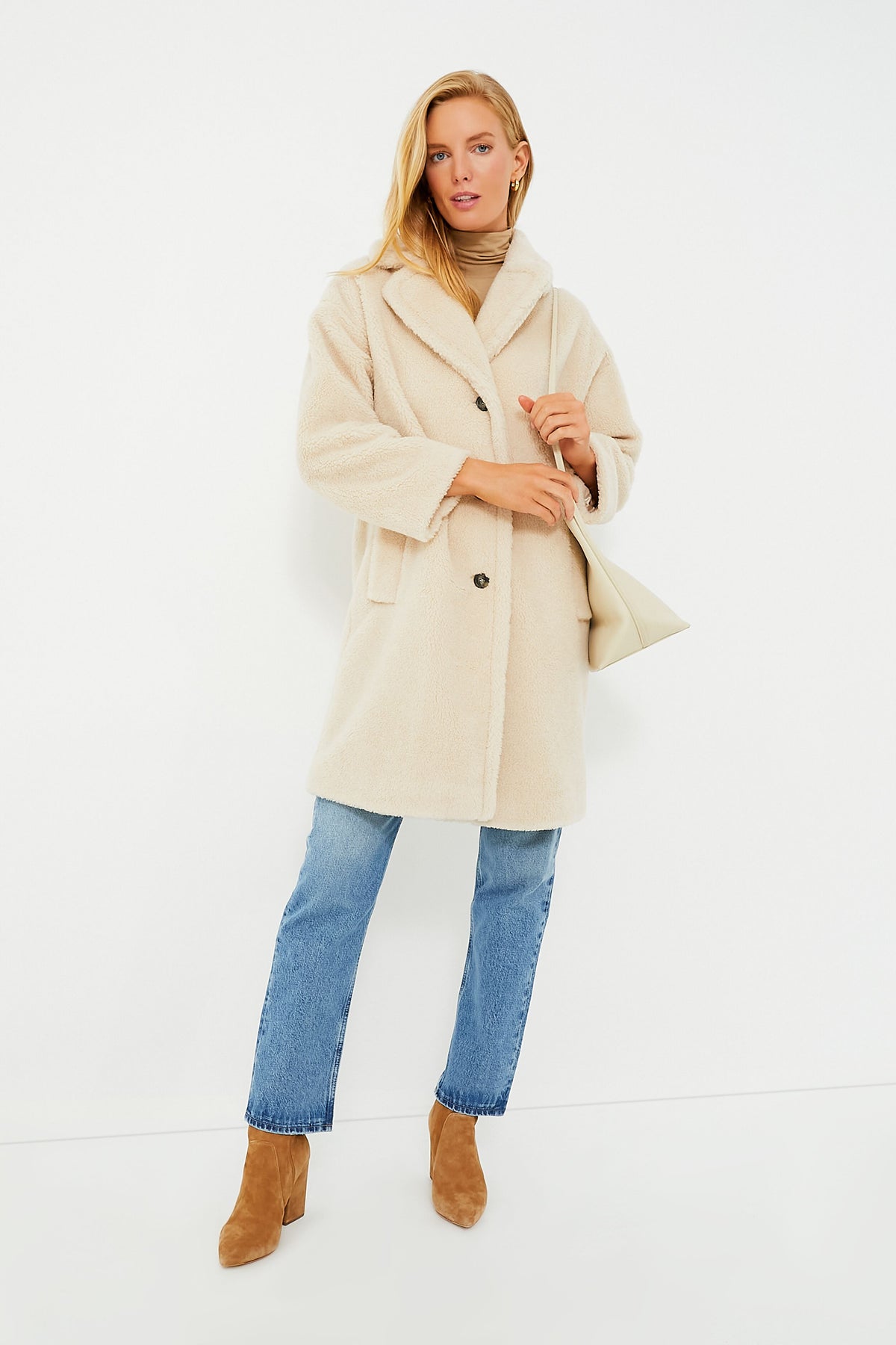 A person wears a beige sherpa coat from Weekend Max Mara, blue jeans, brown heeled boots, a tan top, and carries a cream shoulder bag—embodying the elegance of this Italian lifestyle brand.