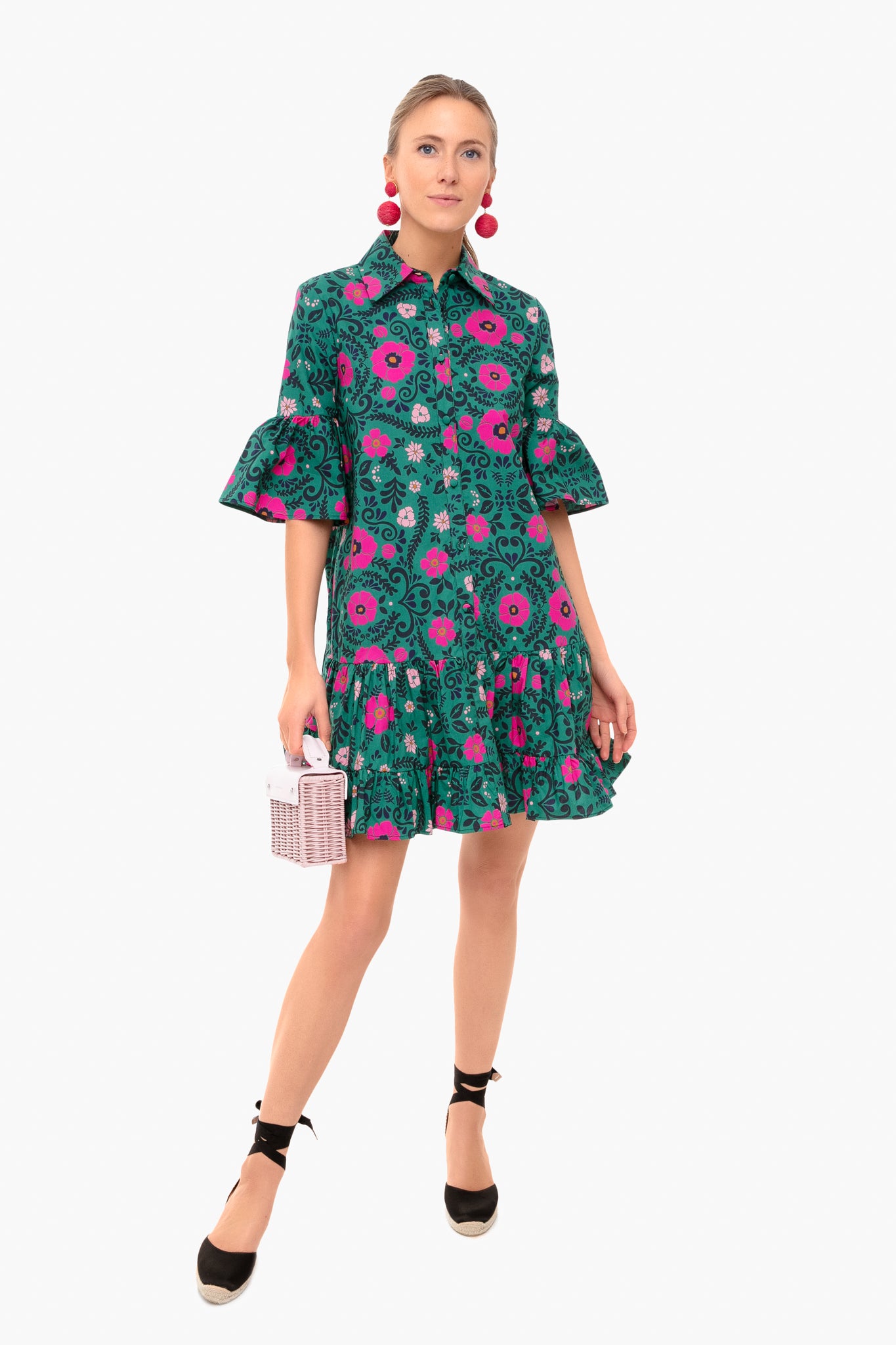 A woman wears a La DoubleJ green cotton poplin dress with pink vintage prints and ruffled sleeves, paired with black ankle-tie shoes and a small white handbag, embodying timeless Italian fashion charm.