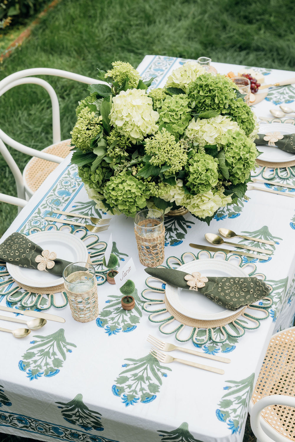 An outdoor table features a SZ Blockprints hand block-printed Indian cotton tablecloth in white and green, gold cutlery, green napkins, elegant glassware, and a vibrant green hydrangea centerpiece.
