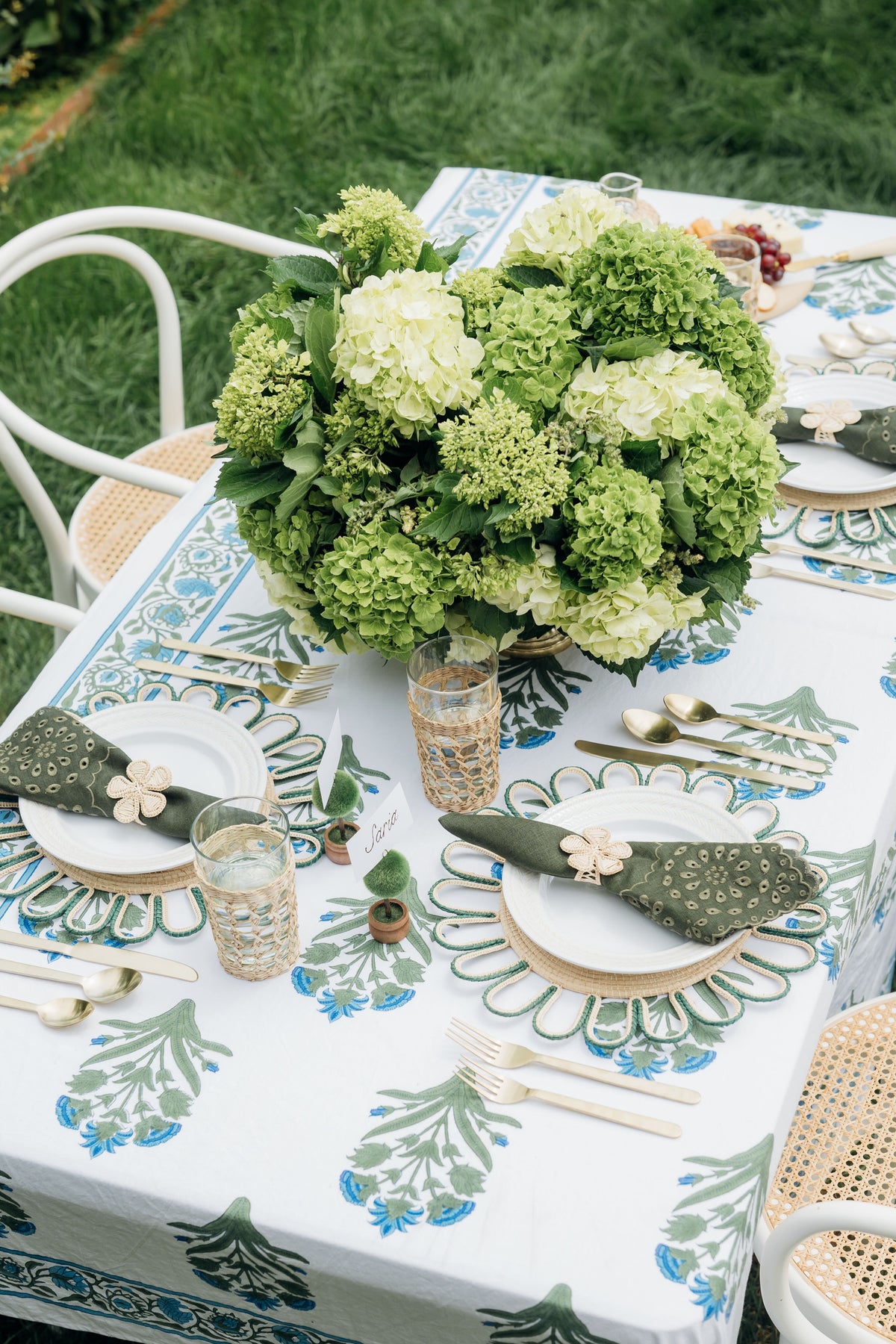 An outdoor table features a SZ Blockprints hand block-printed Indian cotton tablecloth in white and green, gold cutlery, green napkins, elegant glassware, and a vibrant green hydrangea centerpiece.