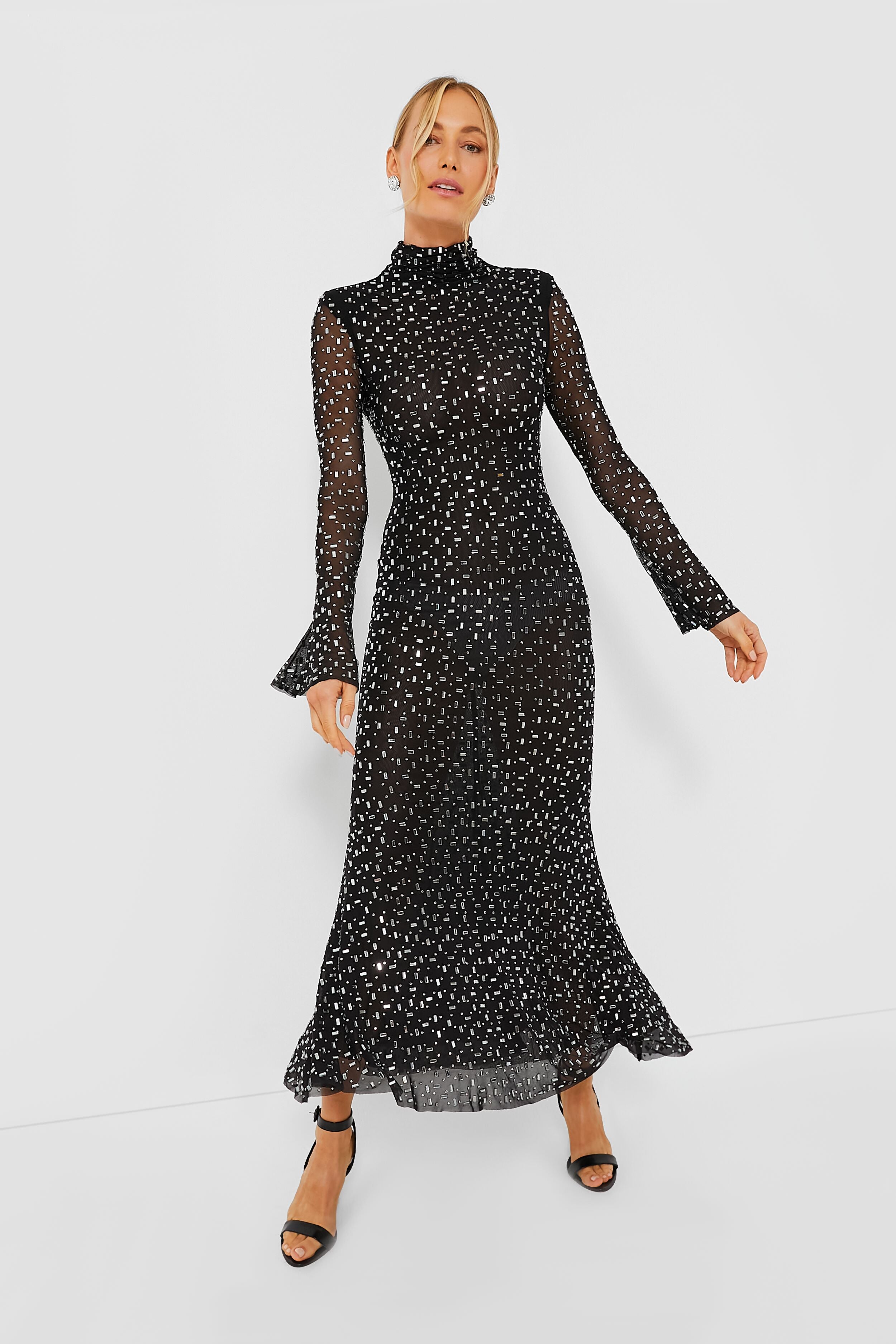 A woman wearing a Self-Portrait black square rhinestone mesh dress with sheer long sleeves, white polka dots, high neck, and ruffled cuffs and hem, styled with black open-toe heels.