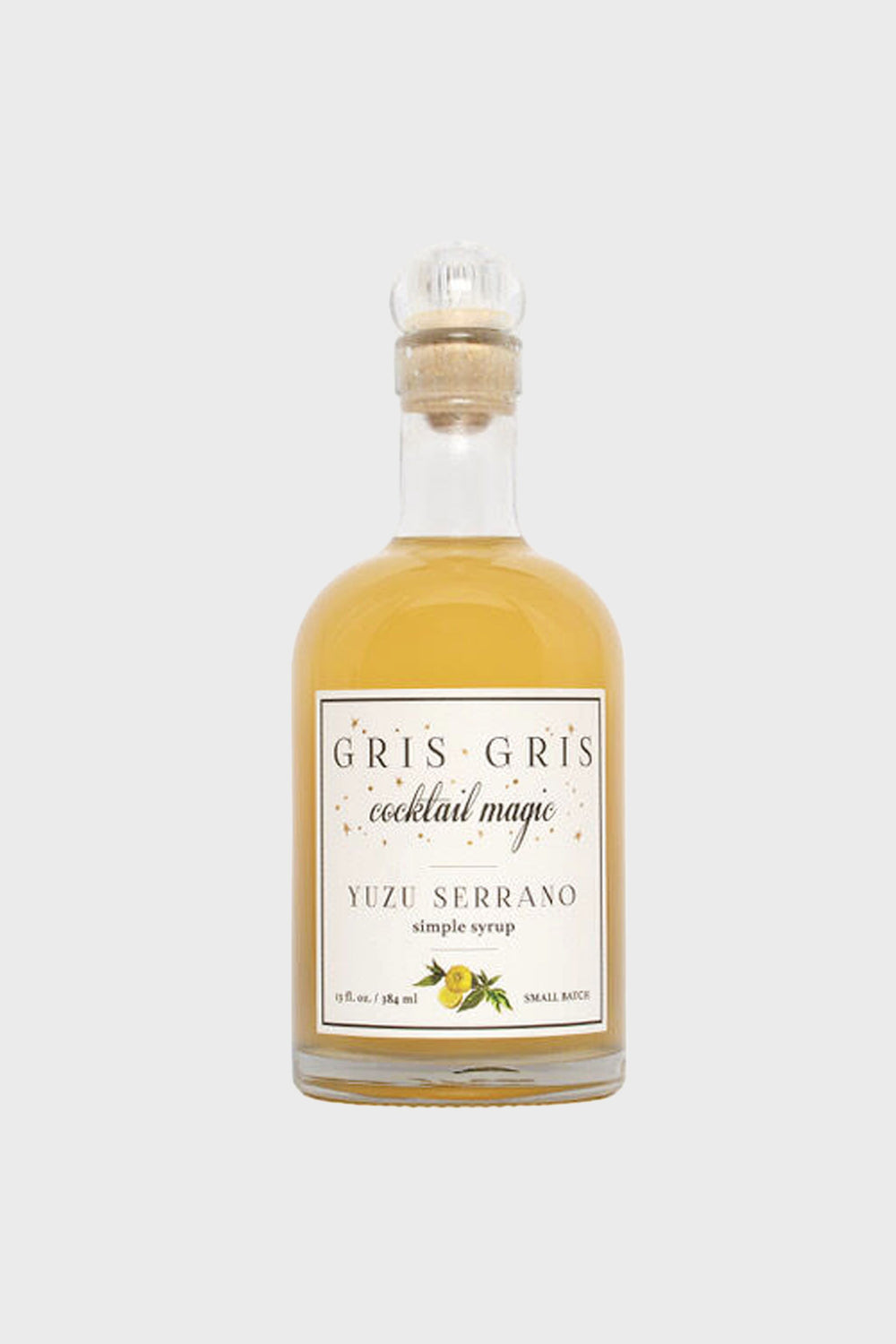 A clear glass bottle from Gris Gris Cocktail Magic, labeled Yuzu Serrano Simple Syrup, with a cork stopper and light amber liquid—an essential ingredient for craft cocktails.