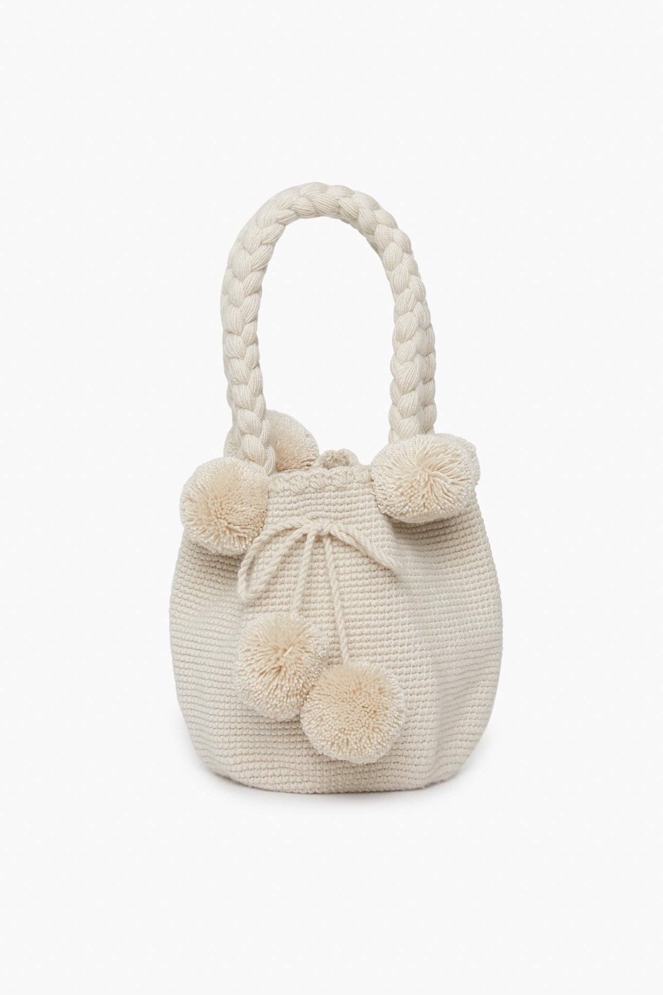 A cream-colored handwoven bag by Marina Orth Foundation from San Jacinto, Colombia, featuring braided handles and decorative pom-poms.