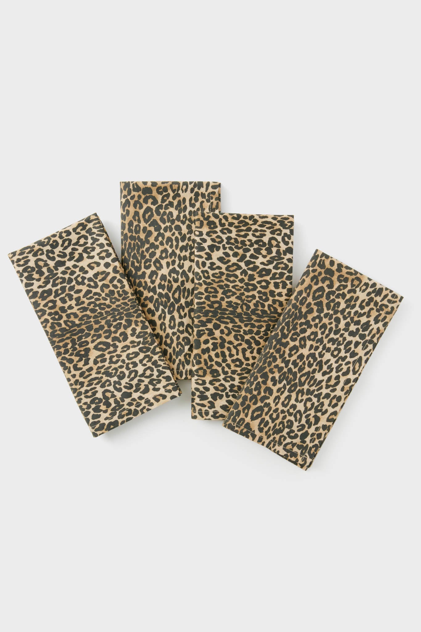 A set of 4 rectangular cotton napkins from Tuckernuck Home features a brown and black leopard print, stylishly arranged in a slightly overlapping display to elevate your table decor.