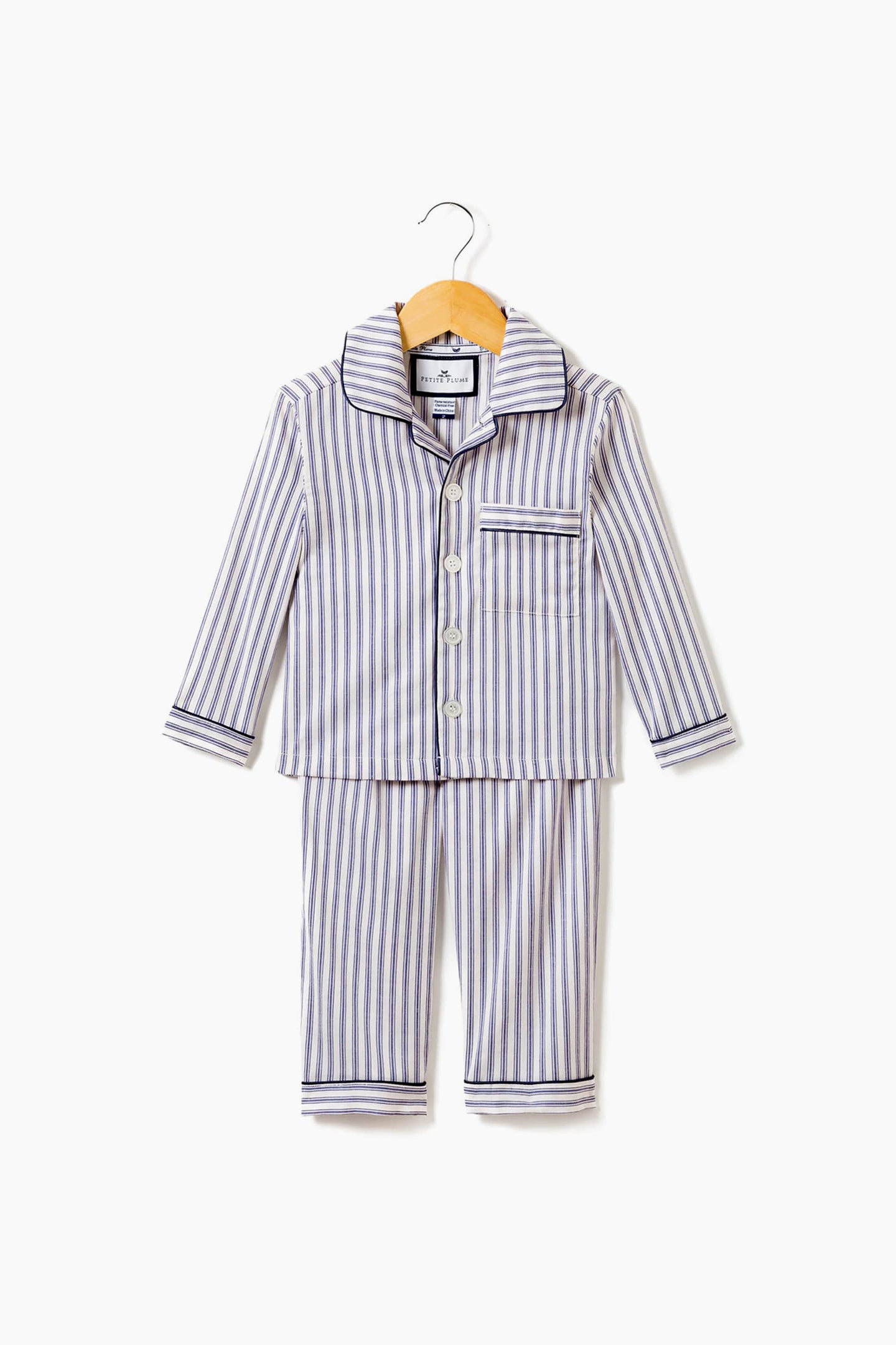 Petite Plume’s children’s navy French ticking pajama set, with long sleeves and pants, is made from cotton for cozy comfort. Shown on a wooden hanger, these pajamas offer soft sleepwear perfect for kids' restful nights.