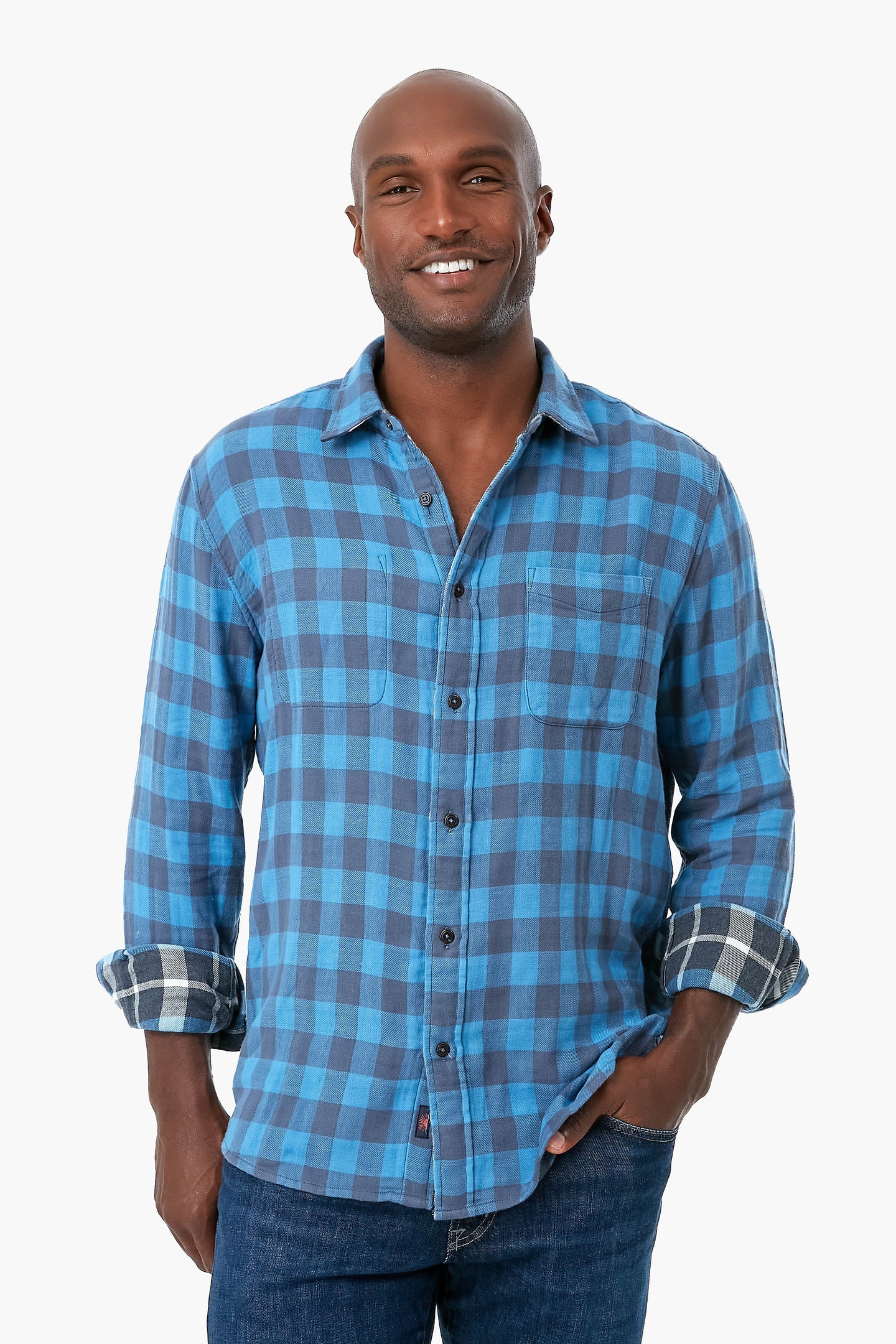 A person in Faherty's blue plaid organic cotton button-up shirt with rolled sleeves and blue jeans, smiling brightly.