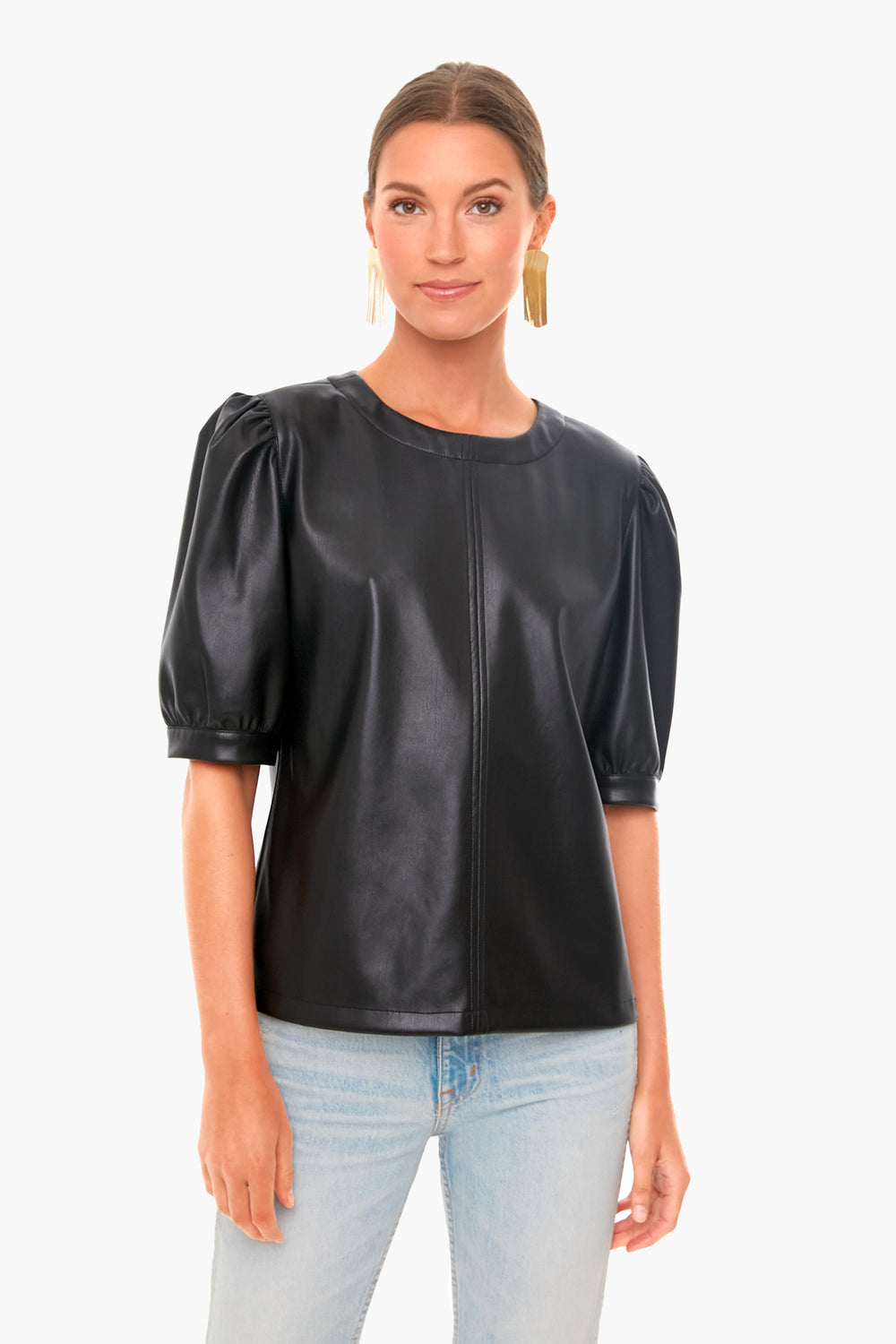 A woman embodies modern glamour in a BB Dakota black vegan leather top with puff sleeves, paired with light blue jeans.