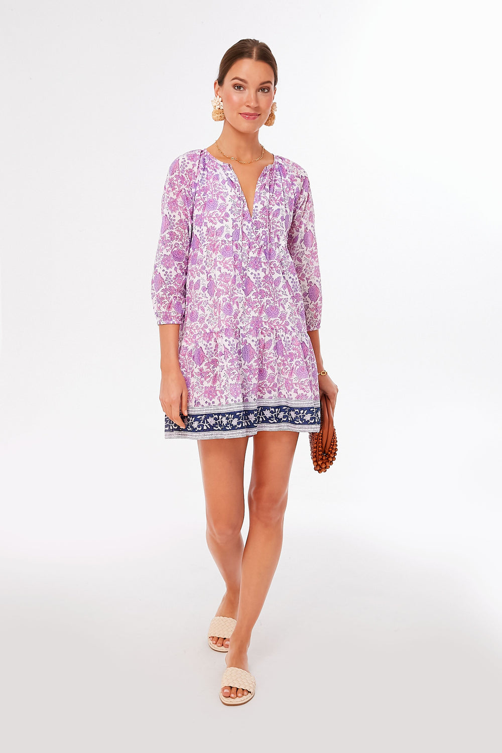 A woman wears an SZ Blockprints light purple block printed dress with three-quarter sleeves, paired with a brown beaded clutch and white sandals.