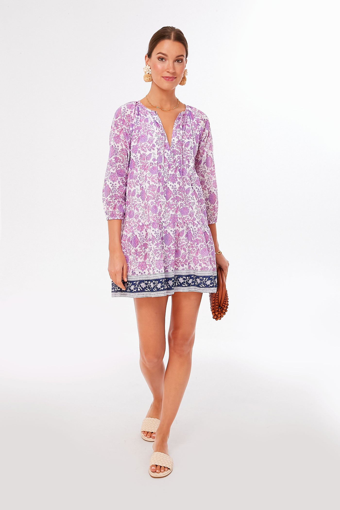 A woman wears an SZ Blockprints light purple block printed dress with three-quarter sleeves, paired with a brown beaded clutch and white sandals.