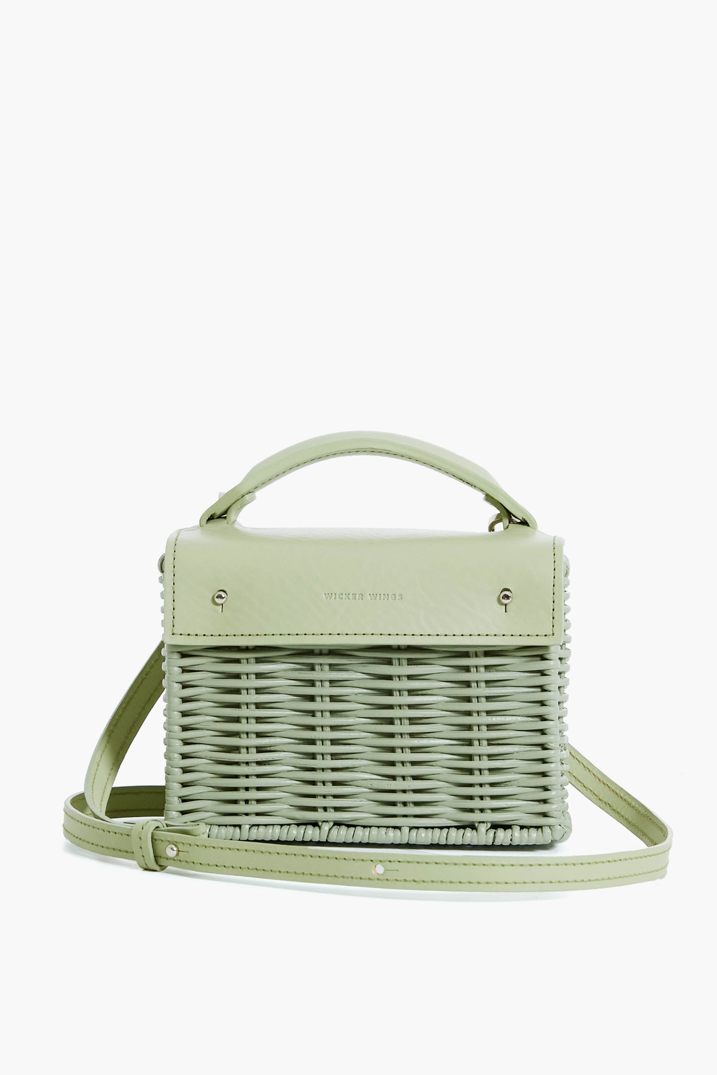 The Wicker Wings light green woven bag features a top handle, leather flap, adjustable shoulder strap, metal accents, and a structured rectangular shape. Made from sustainable materials, it offers modern style with eco-friendly appeal.