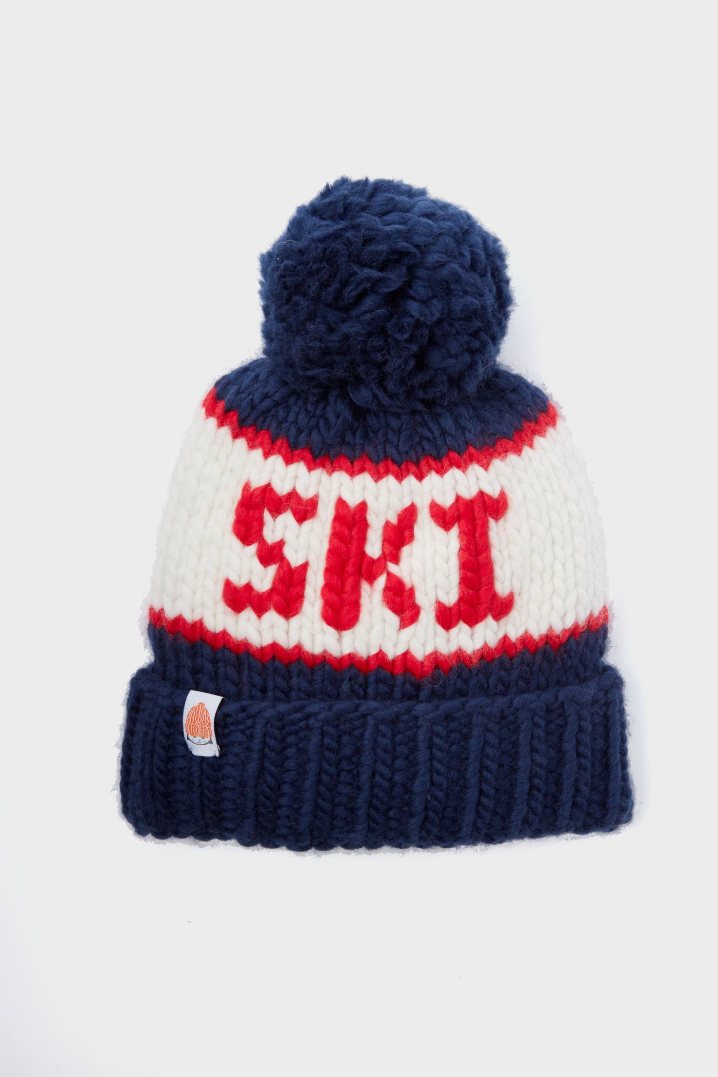 The Sh*t That I Knit beanie is handcrafted from soft Peruvian Merino wool, with a blue pom-pom, blue brim, and SKI in bold red letters with red accents.