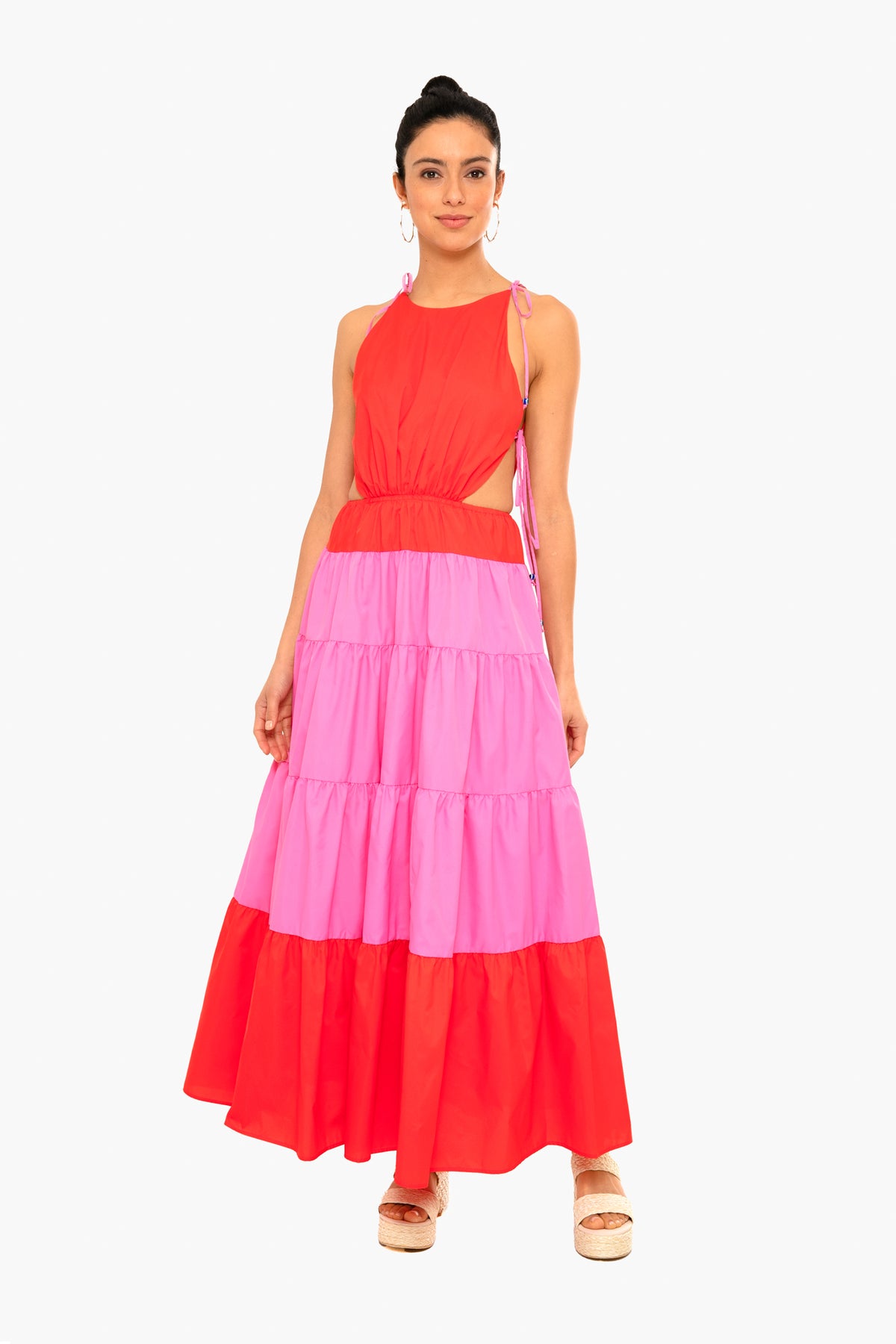 A woman wears the STAUD Minerva Dress, a sleeveless red and pink colorblock maxi with tie shoulders, made from recycled nylon.