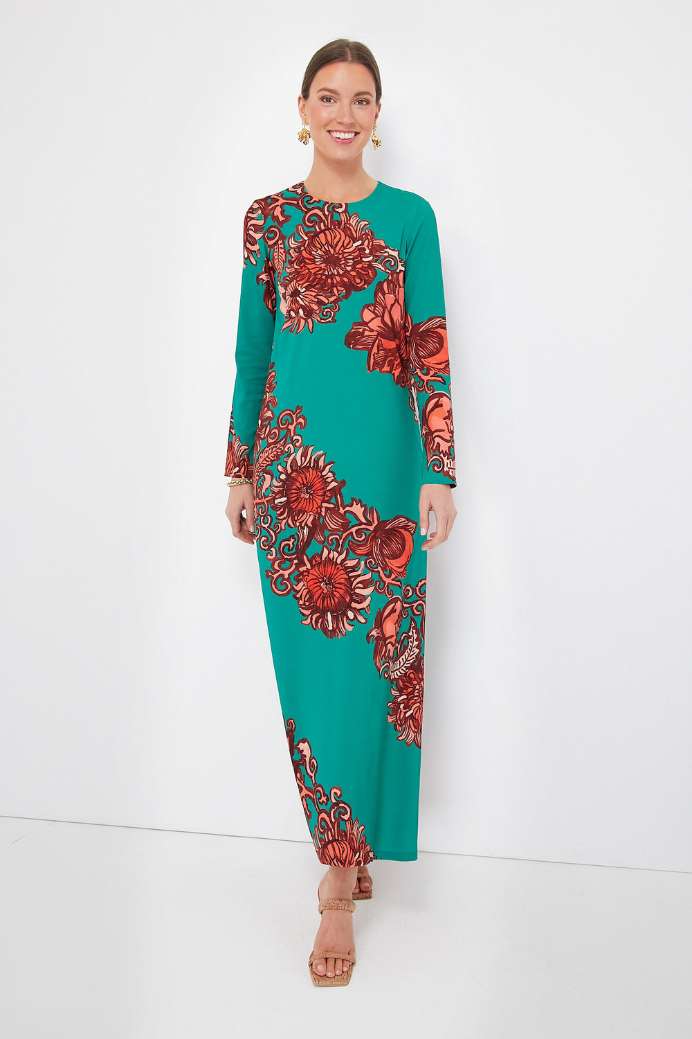 A woman wears a La DoubleJ long sleeve floor-length teal Sablé maxi dress with bold red floral print, tan sandals, and gold earrings.