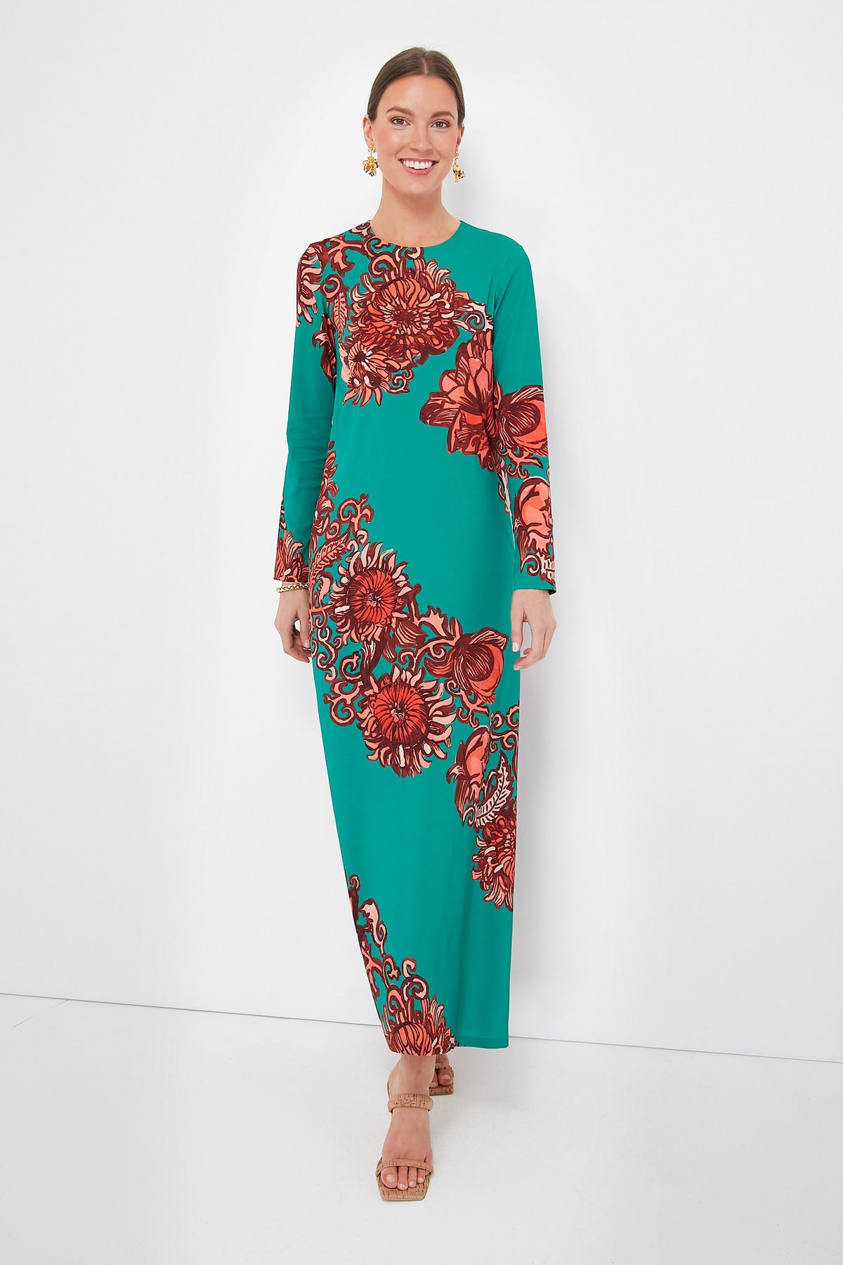 A woman wears a La DoubleJ long sleeve floor-length teal Sablé maxi dress with bold red floral print, tan sandals, and gold earrings.