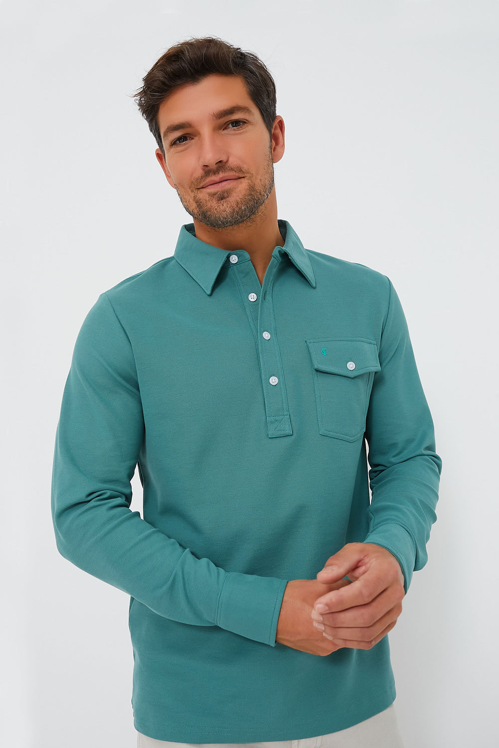 A man stands against a plain white background wearing a teal Criquet Long Sleeve Players Shirt crafted from Peruvian Pima Cotton, featuring a chest pocket.