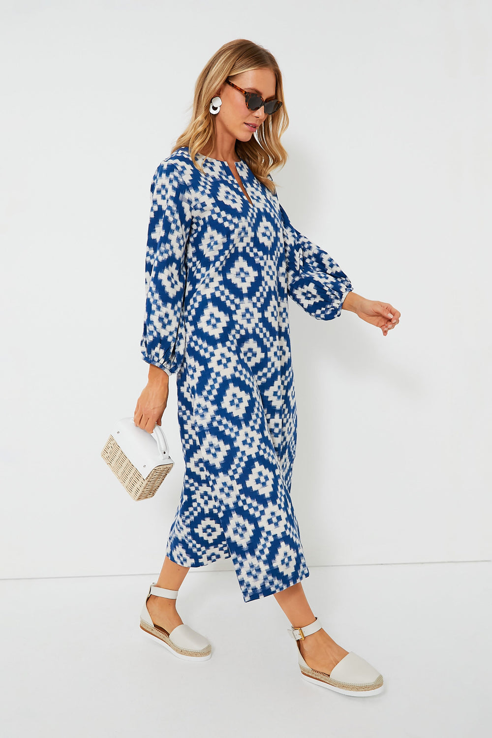 A woman wears the KLEED Blue Dorcas Kaftan in IKAT cotton, paired with sunglasses, white earrings, beige espadrille sandals, and a small white handbag—a sustainable loungewear look that’s effortlessly chic.