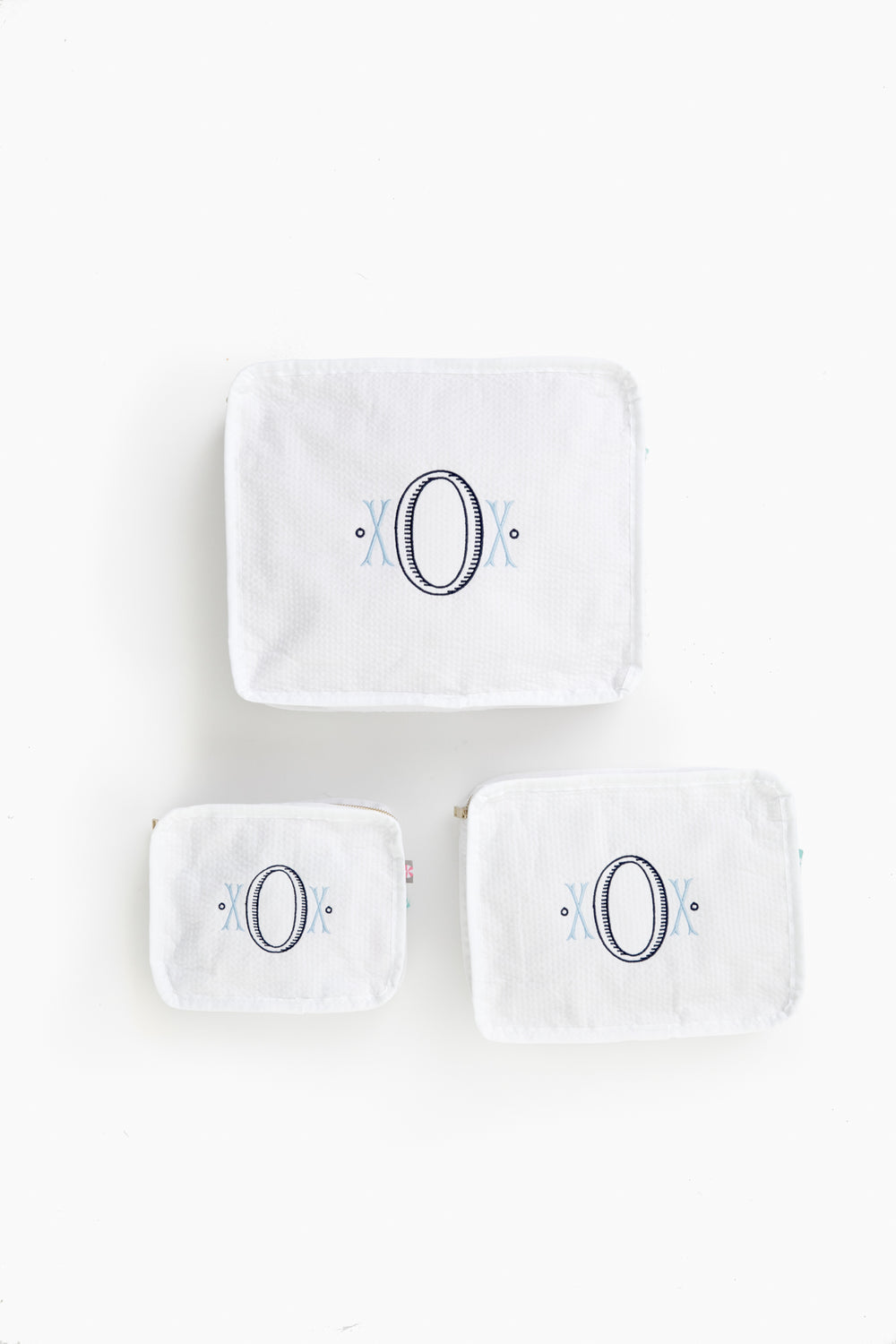 Three white seersucker travel pouches by Caton's Wharf, each in a different size with a large embroidered letter O and blue accents—ideal as a bridesmaids gift.