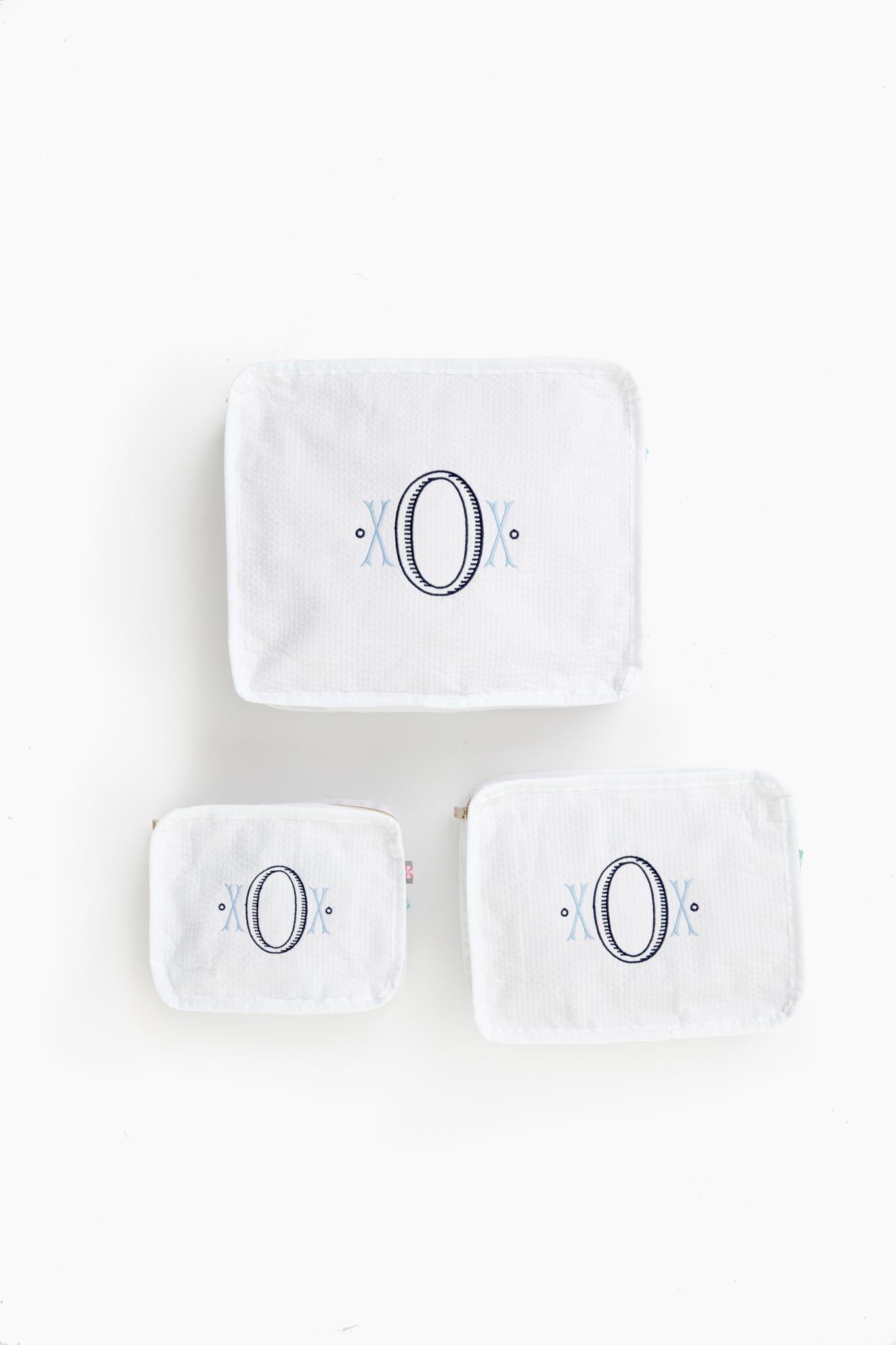Three white seersucker travel pouches by Caton's Wharf, each in a different size with a large embroidered letter O and blue accents—ideal as a bridesmaids gift.