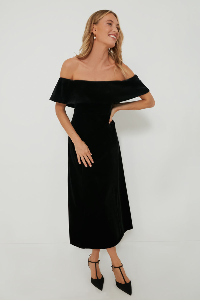 A woman poses confidently with one hand on her hip, wearing a Pomander Place off-the-shoulder black velvet midi dress and black heels.