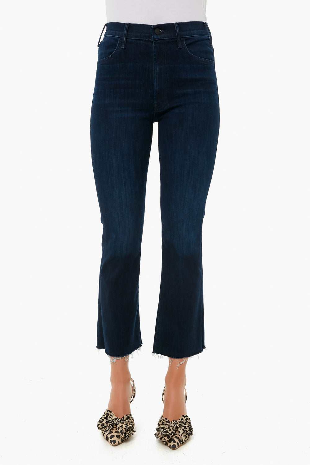 A person wears MOTHER dark blue cropped ankle jeans with a raw hem, paired with leopard print heels, highlighting the brand’s stylish denim fit.