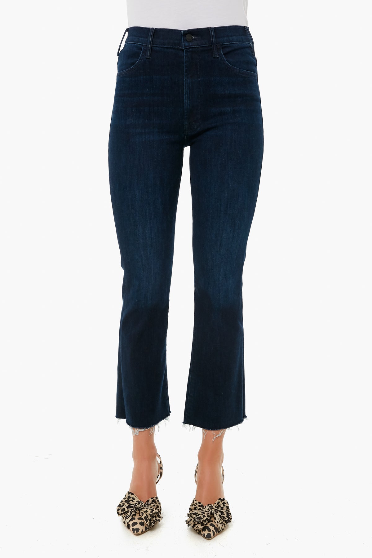 A person wears MOTHER dark blue cropped ankle jeans with a raw hem, paired with leopard print heels, highlighting the brand’s stylish denim fit.