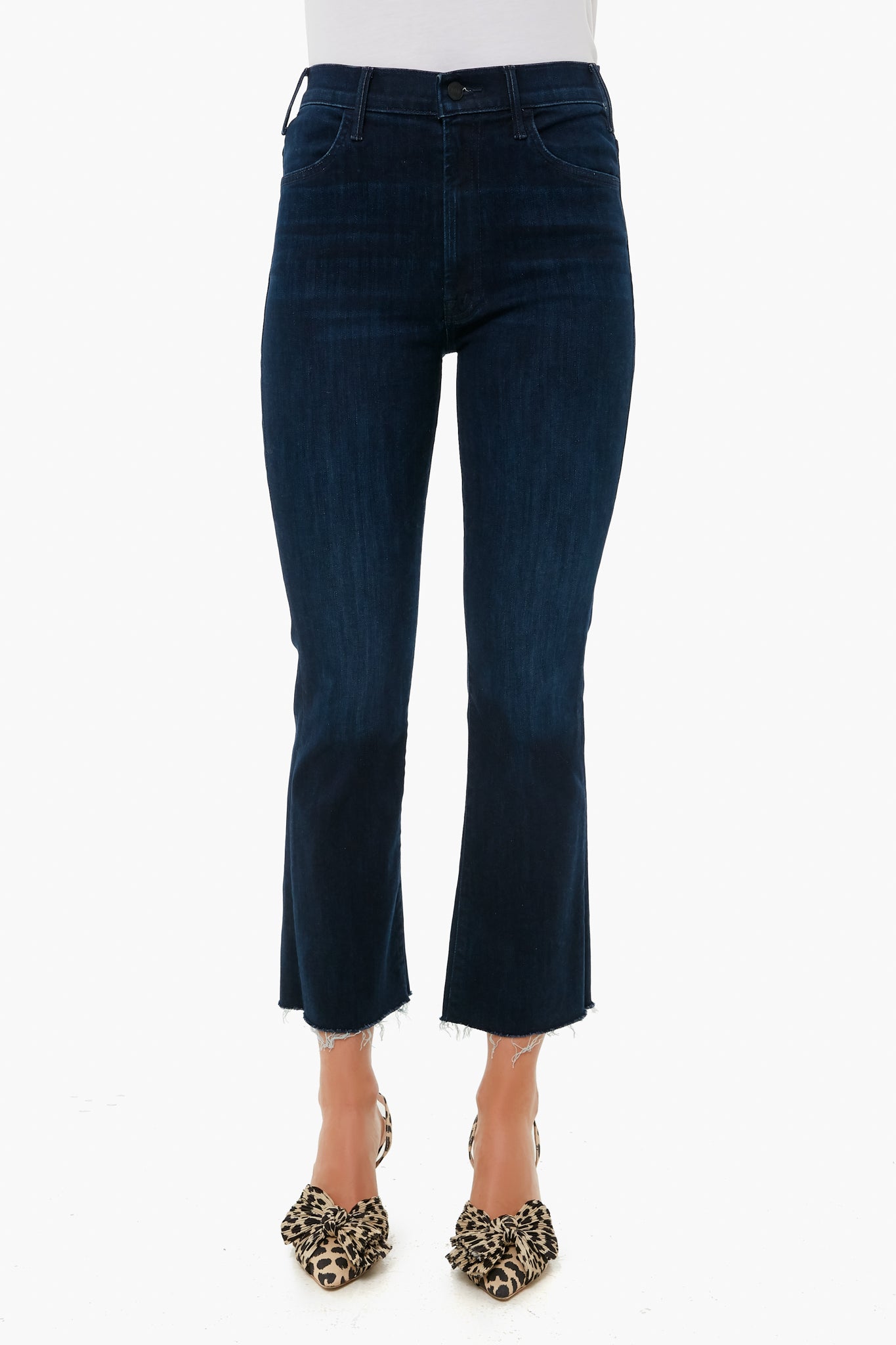 A person wears MOTHER dark blue cropped ankle jeans with a raw hem, paired with leopard print heels, highlighting the brand’s stylish denim fit.