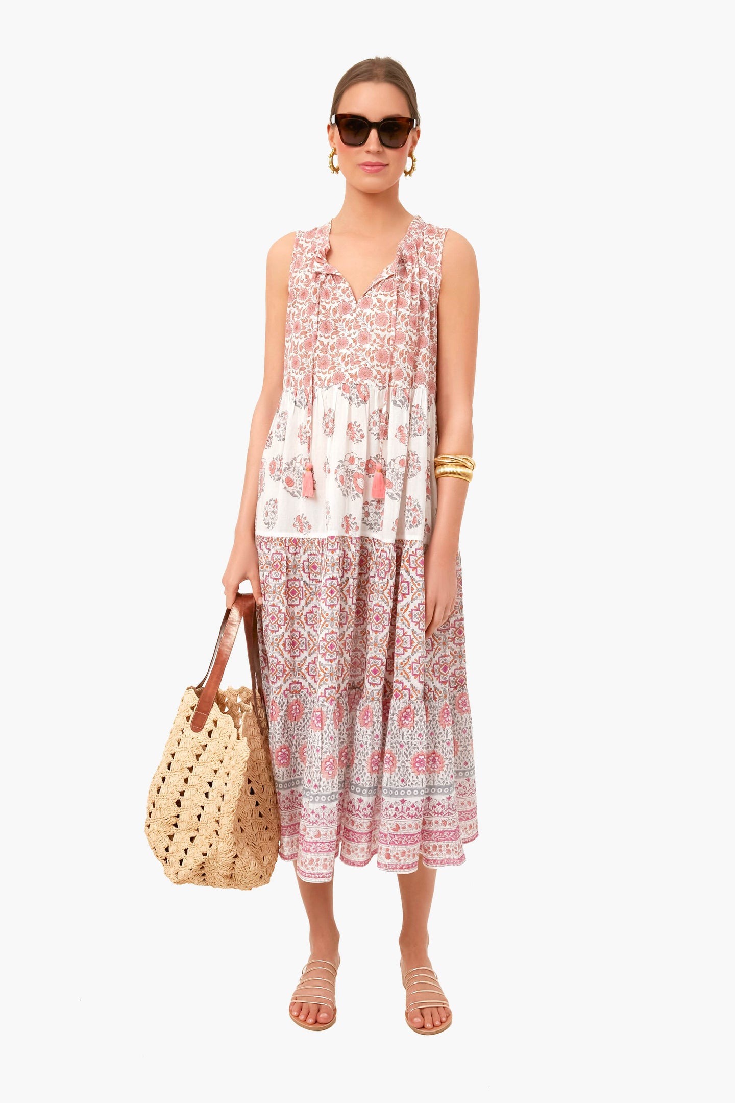 A woman in sunglasses, a boho-chic sleeveless patterned Tnuck Beach midi dress, and sandals holds a woven tote bag.