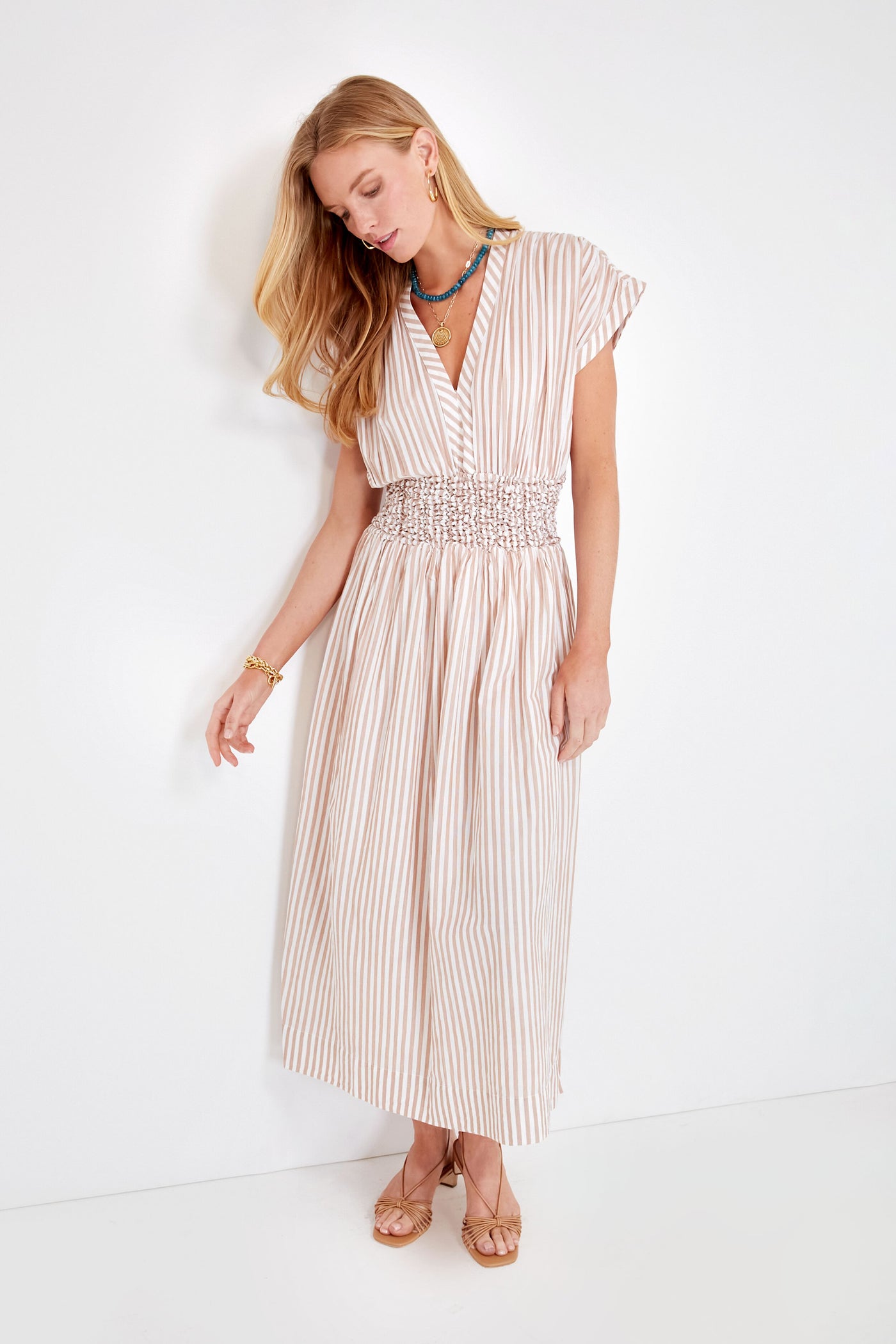 A woman wears a MIRTH light-colored, short-sleeve, ankle-length striped cotton maxi dress with a smocked waist and tan sandals—an ideal choice for ethical resort wear.