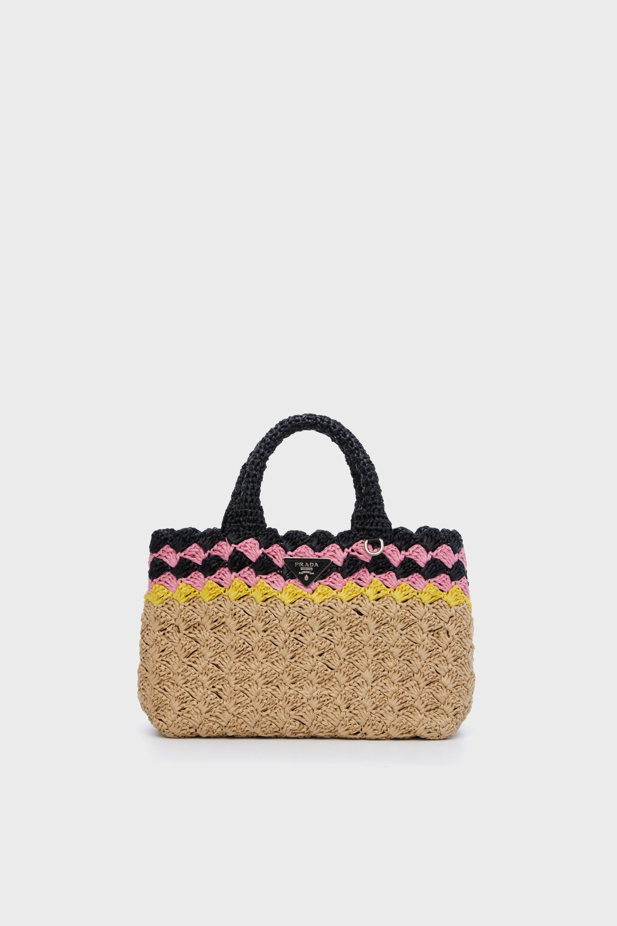 The Tuckernuck Archive Collection luxury tote bag features short handles, a natural beige woven base, and decorative pink, black, and yellow bands near the top.