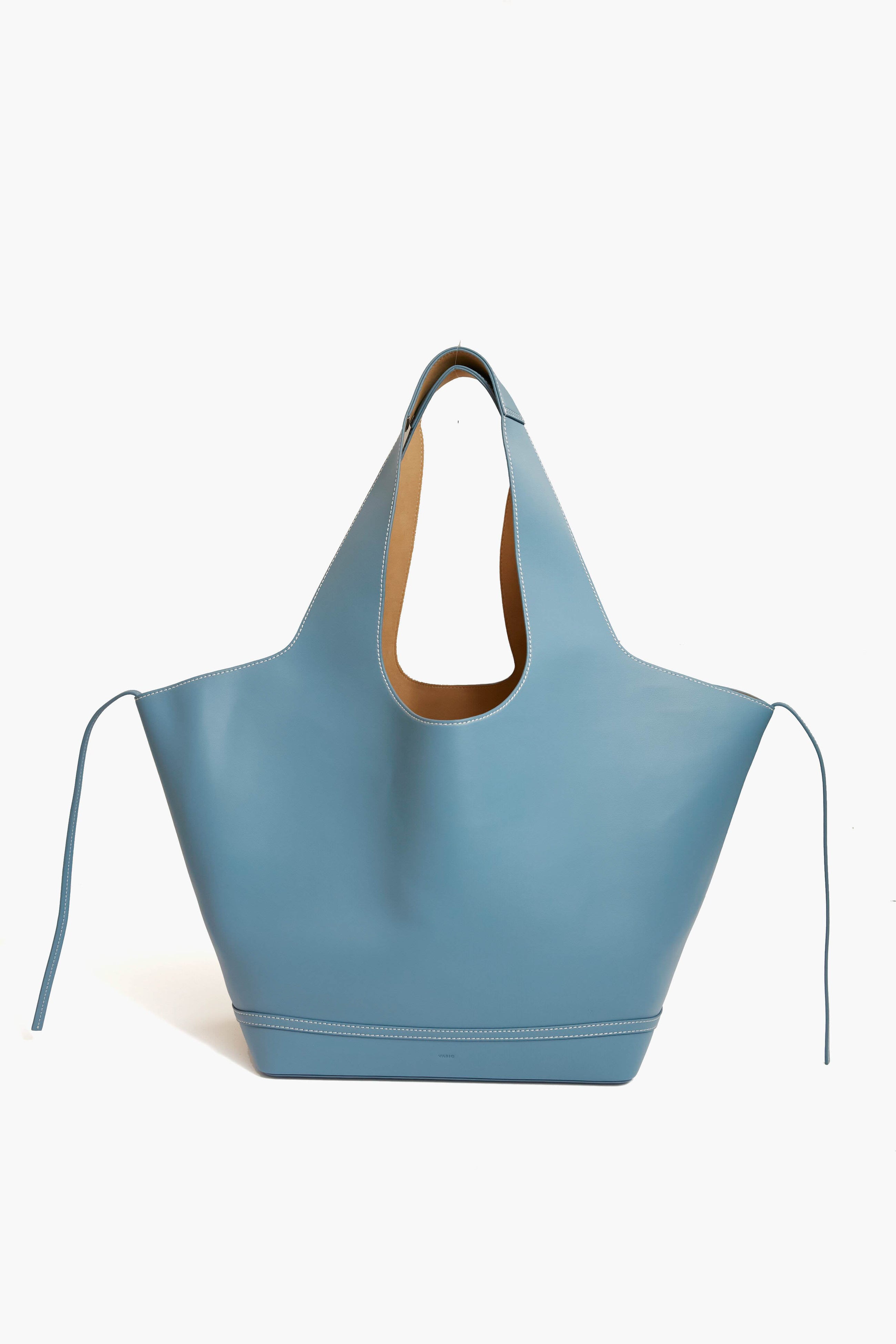 The Vasic Aqua Mask Tote is a large, light blue leather tote bag featuring a cut-out handle and extended side panels—perfect for everyday use.