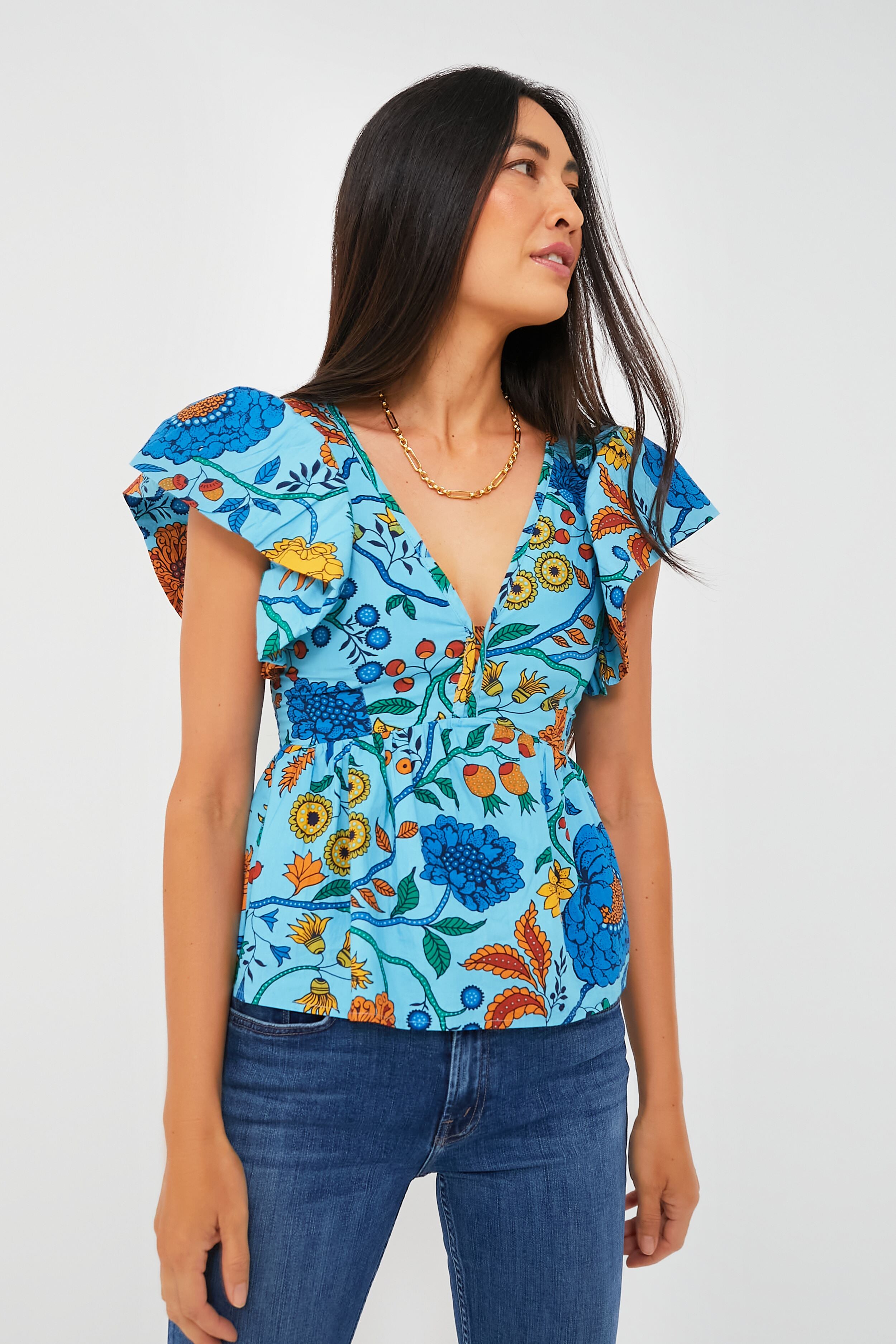 A woman wears a vibrant floral top by Love the Label, featuring ruffle sleeves, a V-neck, and a fitted waist, paired with blue jeans.