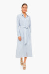 A woman wears a chic and versatile Tuckernuck Caldwell dress in blue and white stripes with a tie belt, paired with beige sandals and statement earrings.