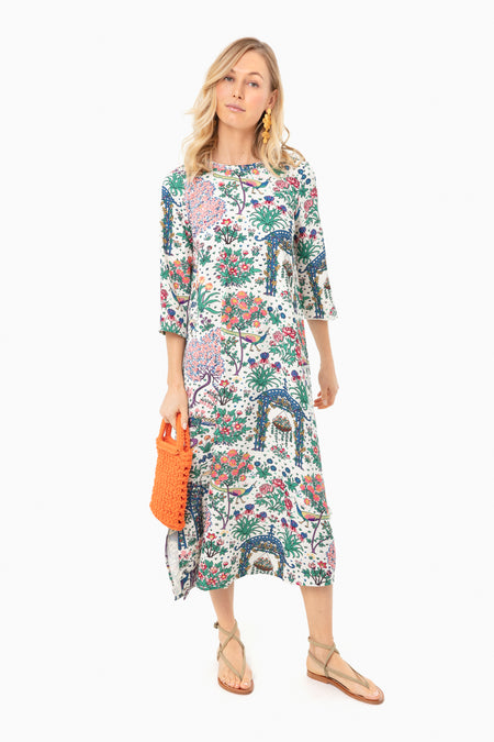 A woman wears a Tuckernuck garden print midi dress with quarter sleeves, tan sandals, orange earrings, and holds an orange woven handbag.