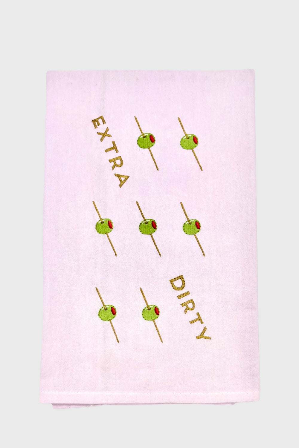 A unique gift: the Lynen embroidered tea towel showcases green olives on toothpicks and “EXTRA DIRTY” diagonally across soft white fabric.