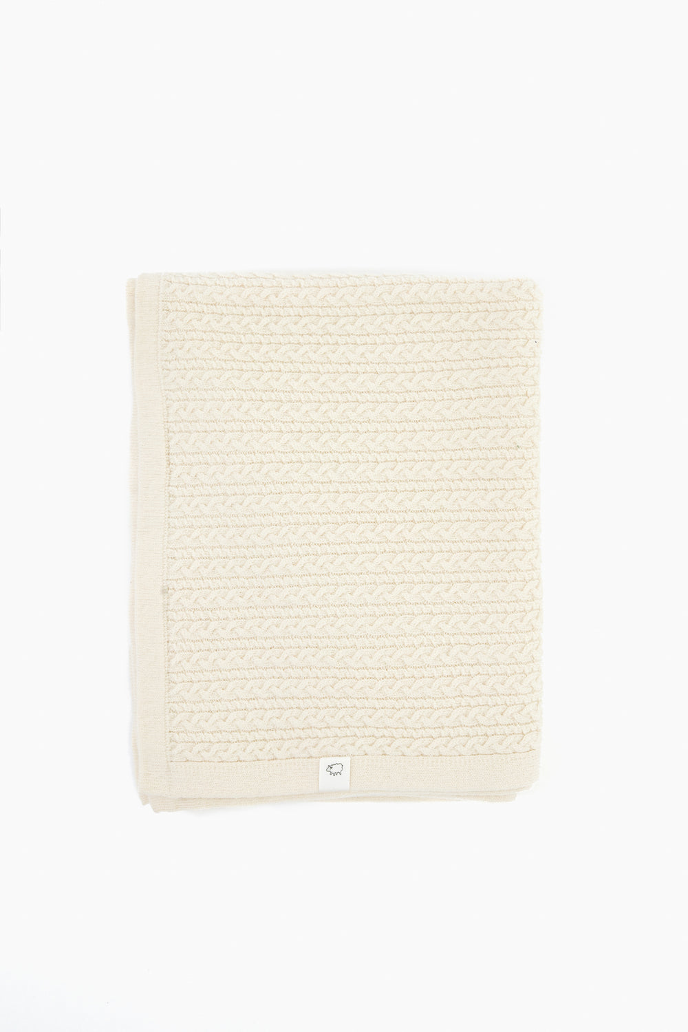 A folded cream-colored knit blanket with a textured pattern and a small white label on the edge, crafted from Hudson Valley Cormo wool by baa for luxury heirloom knits.