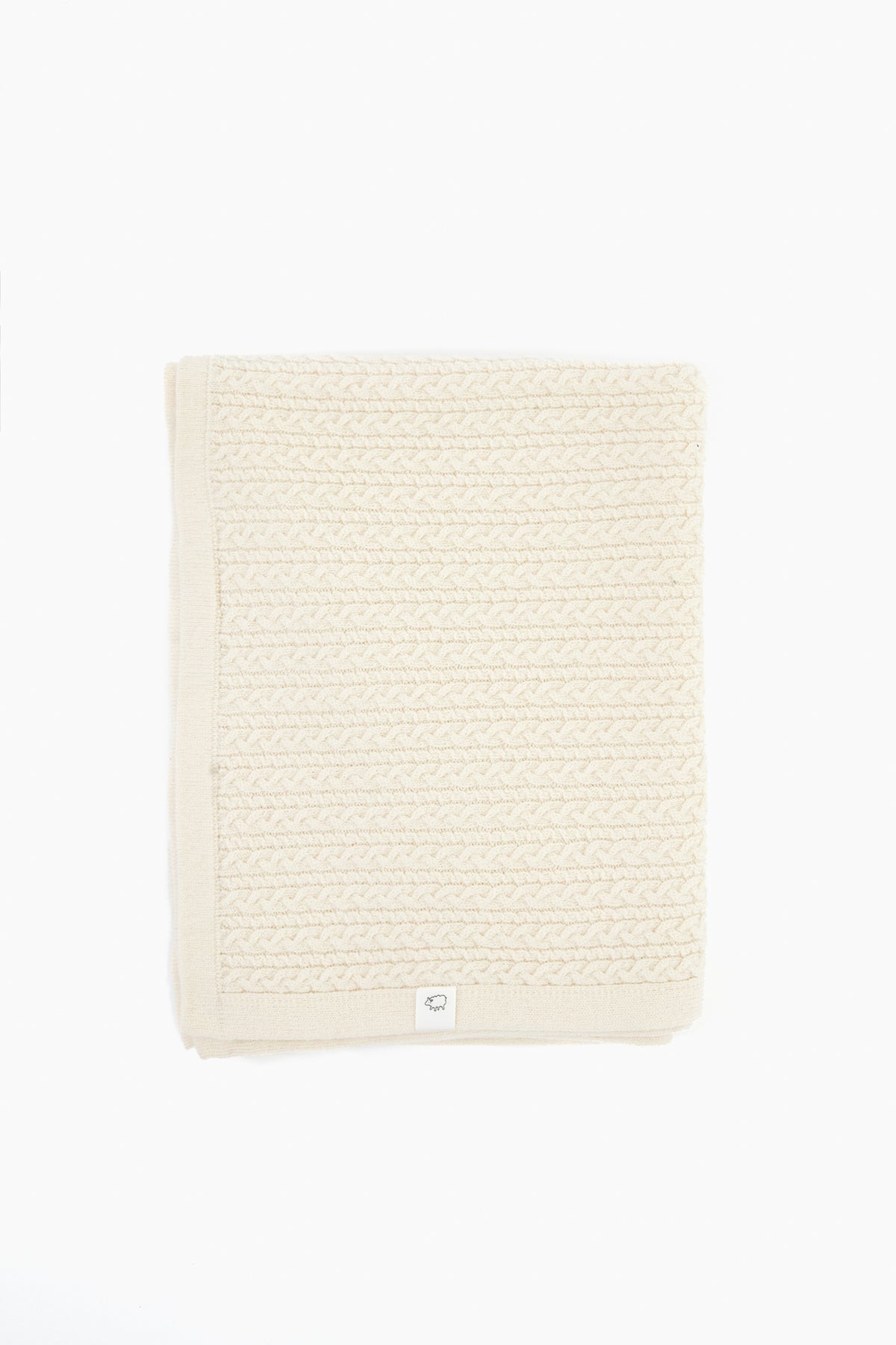 A folded cream-colored knit blanket with a textured pattern and a small white label on the edge, crafted from Hudson Valley Cormo wool by baa for luxury heirloom knits.
