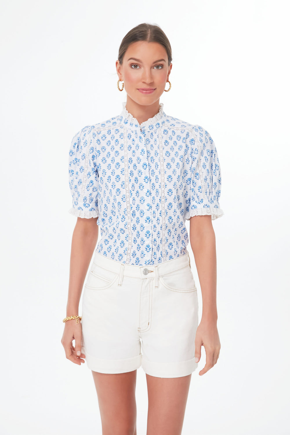 A woman models a Pink City Prints handmade blouse with blue floral patterns and white shorts, standing gracefully to showcase the elegant organic cotton fabric.