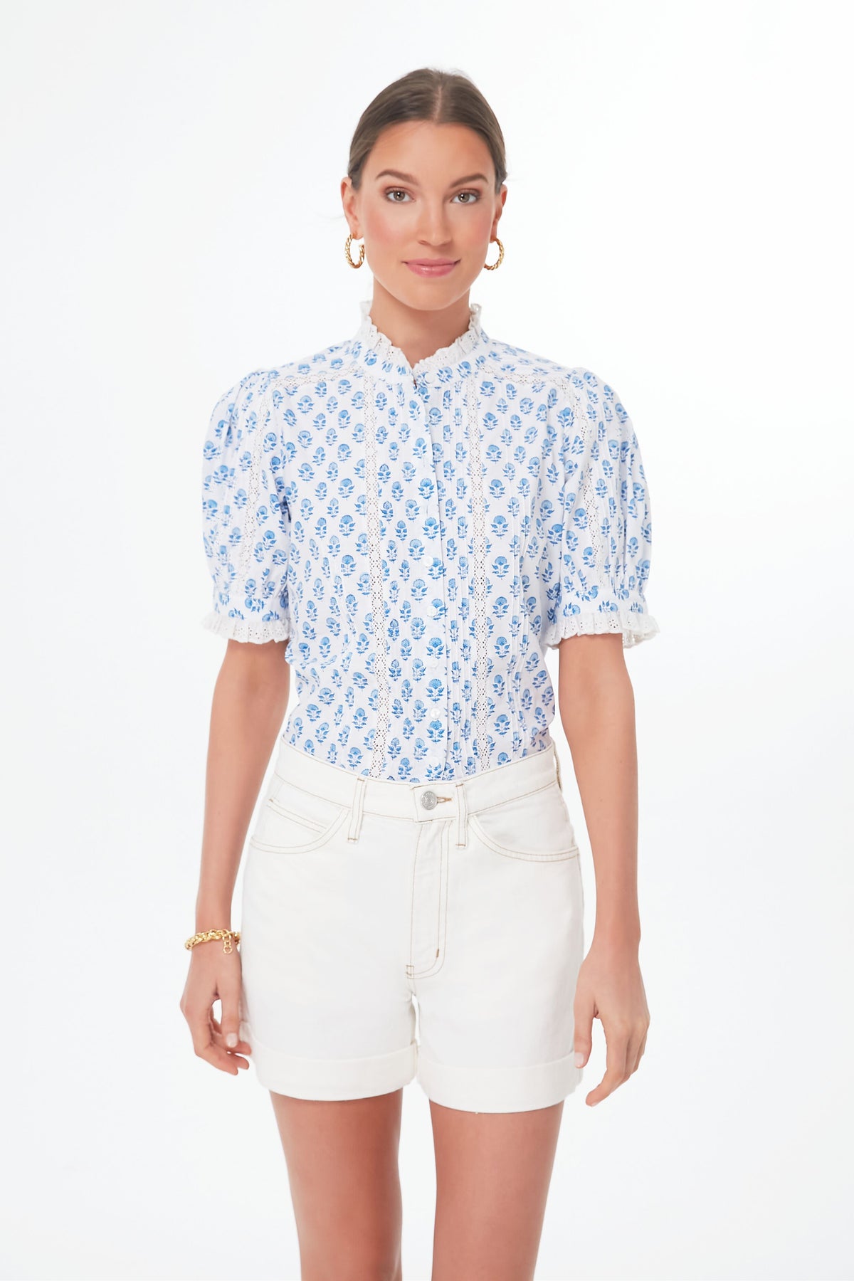 A woman models a Pink City Prints handmade blouse with blue floral patterns and white shorts, standing gracefully to showcase the elegant organic cotton fabric.