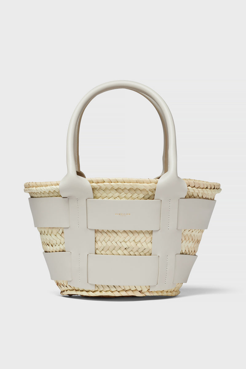The Demellier woven straw raffia bag features wide white leather straps and handles, making it a chic mini tote perfect for everyday use.