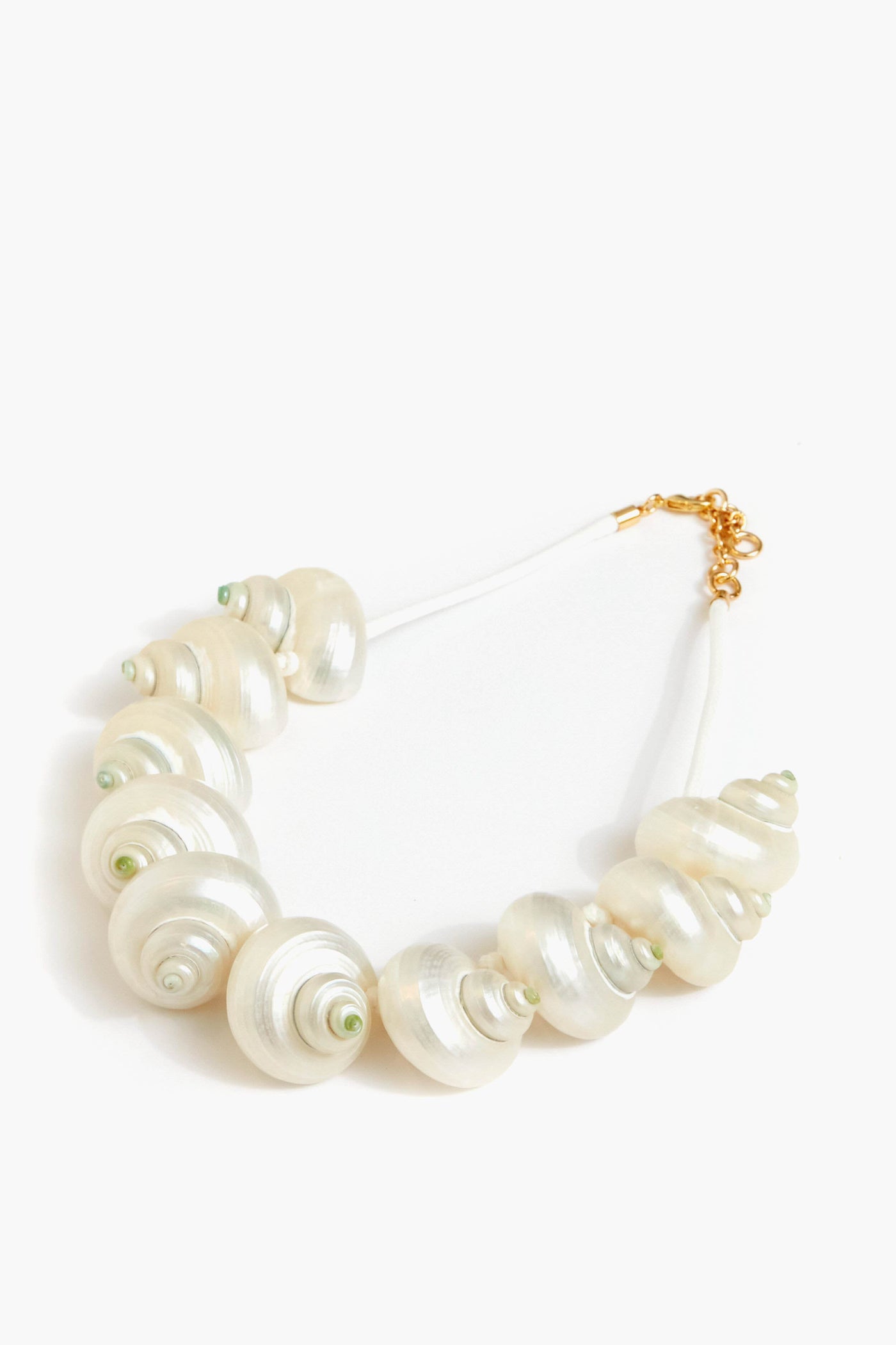 The Tuckernuck Jewelry Calypso Necklace features large glossy white shell-shaped beads, small green accents, real conch shell details, a white cord, and a 14K gold-plated clasp.