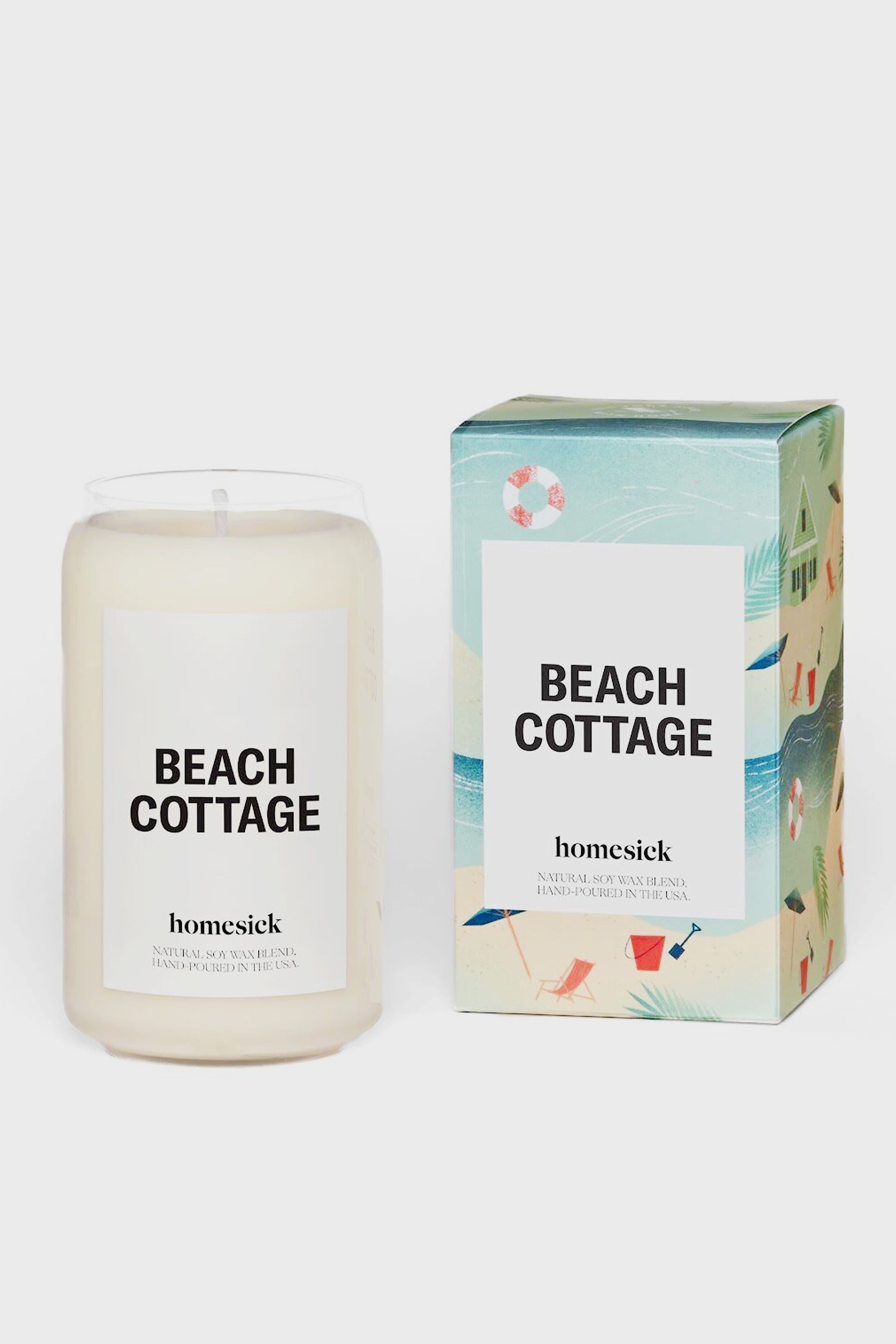 A Homesick Candles Beach Cottage candle made with natural soy wax sits next to its box, both adorned with beach-themed illustrations and the BEACH COTTAGE label for a charming home fragrance.