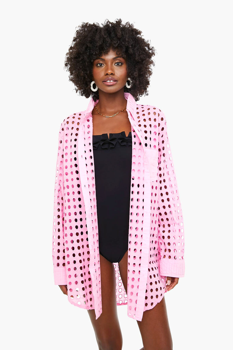 A woman wears a Solid & Striped black one-piece swimsuit with an oversized pink perforated button-up shirt styled as a beach coverup, standing facing forward.