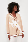 A woman styles a Tuckernuck oversized lobster cardigan with brown trim and a bold white lobster motif, pairing it with layered necklaces for a chic, preppy look.